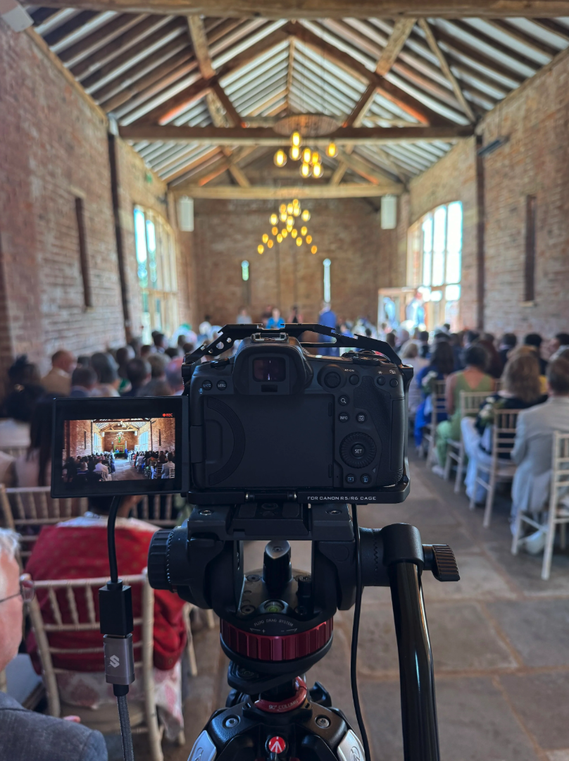 Camera live streaming a wedding ceremony inside a rustic brick building with chandeliers and guests in formal attire.