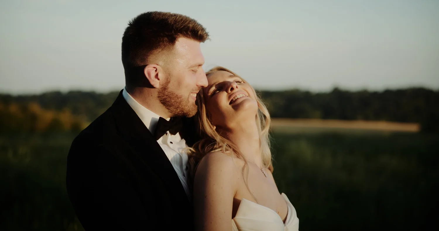 A groom kissing his smiling bride outdoors on their wedding day