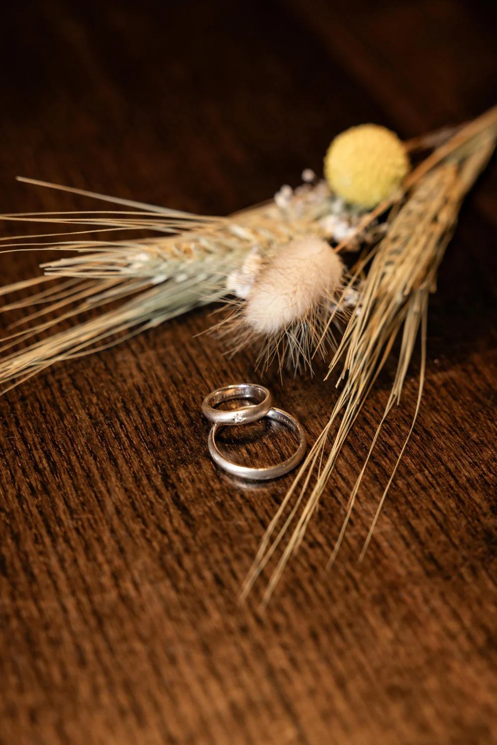 Wedding rings beside dried flowers on a wooden table