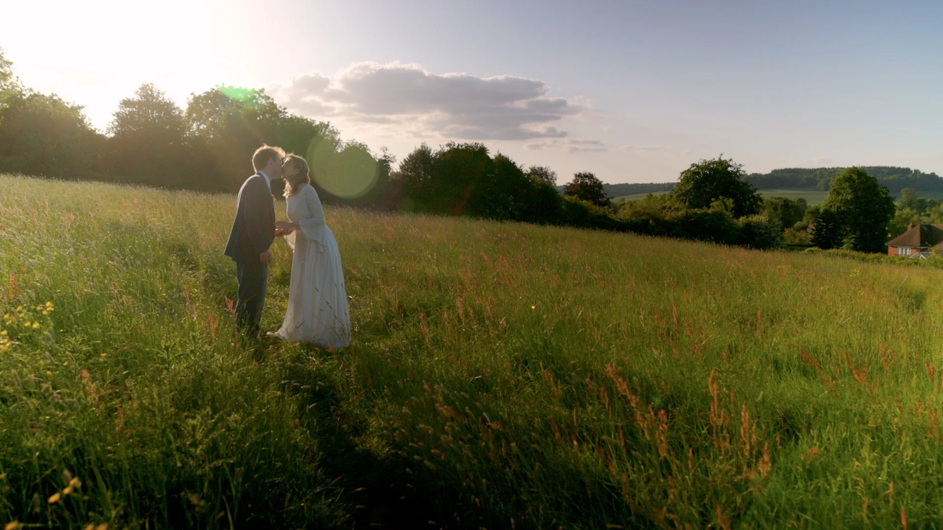 A couple dressed as a bride and groom stand in a grassy field during sunset, facing each other closely in a romantic pose. A perfect photo spot at Kings Chapel, Old Amersham