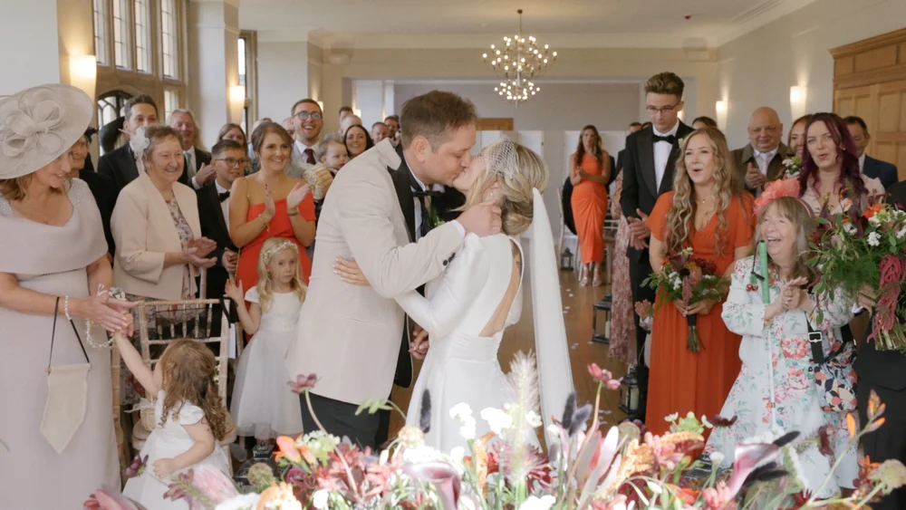 Newlyweds sharing a kiss as their wedding guests celebrate