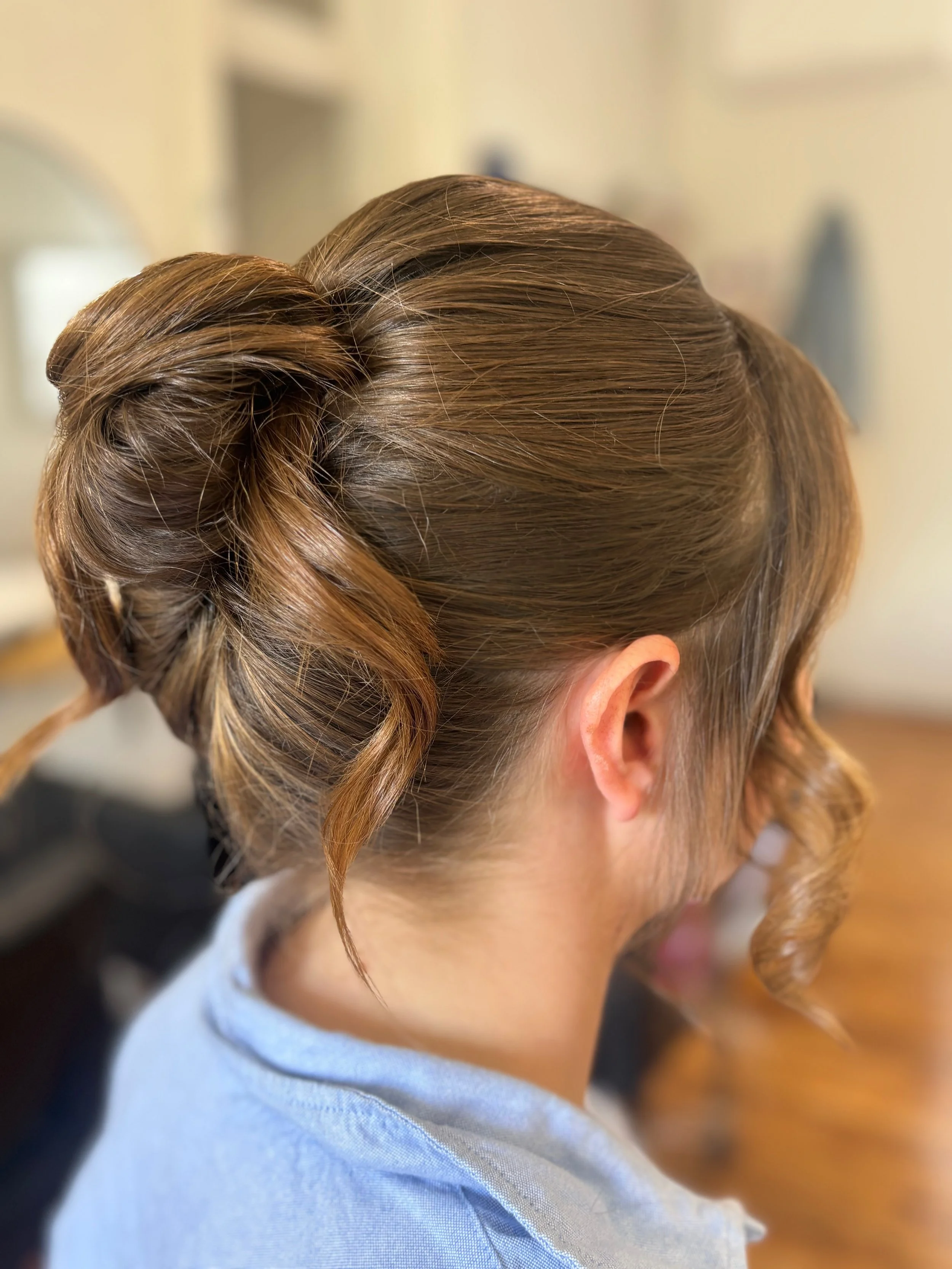 Side view of a woman with styled brown hair, with an elegant updo and loose curls hanging down.