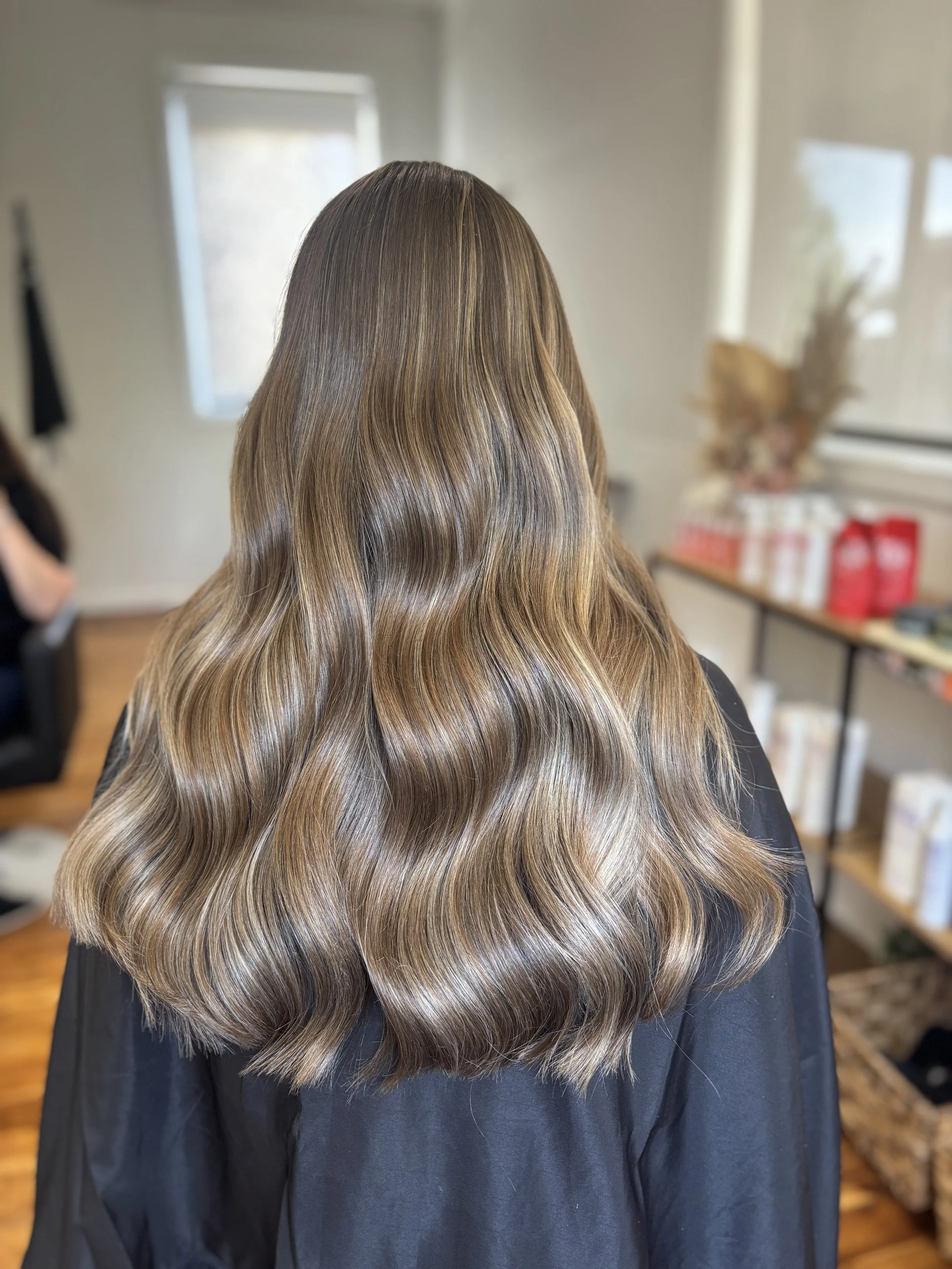 Back of woman with long, wavy, light brown hair in a salon.