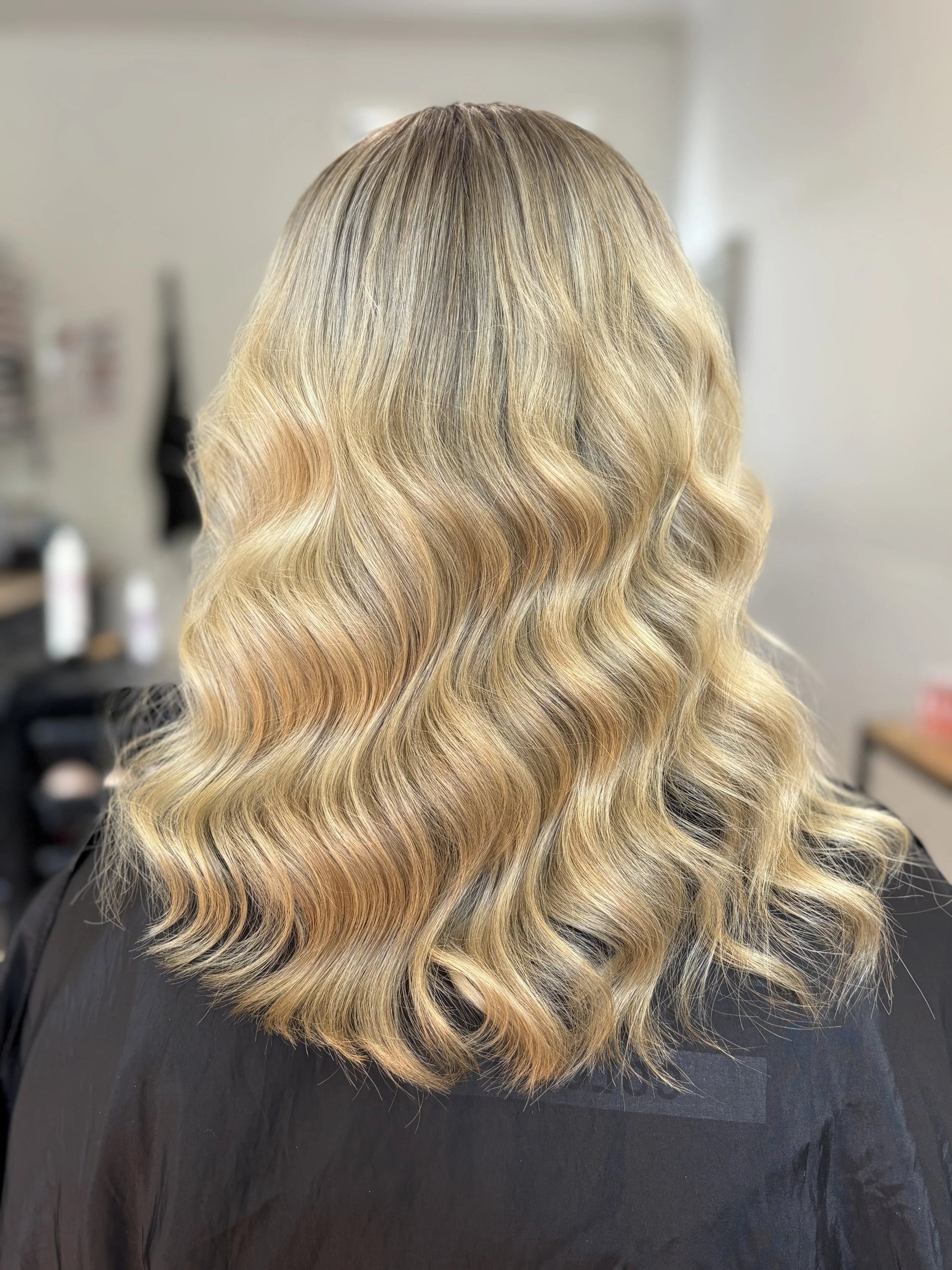 Back of a woman's head showing shoulder-length blonde hair with loose curls.