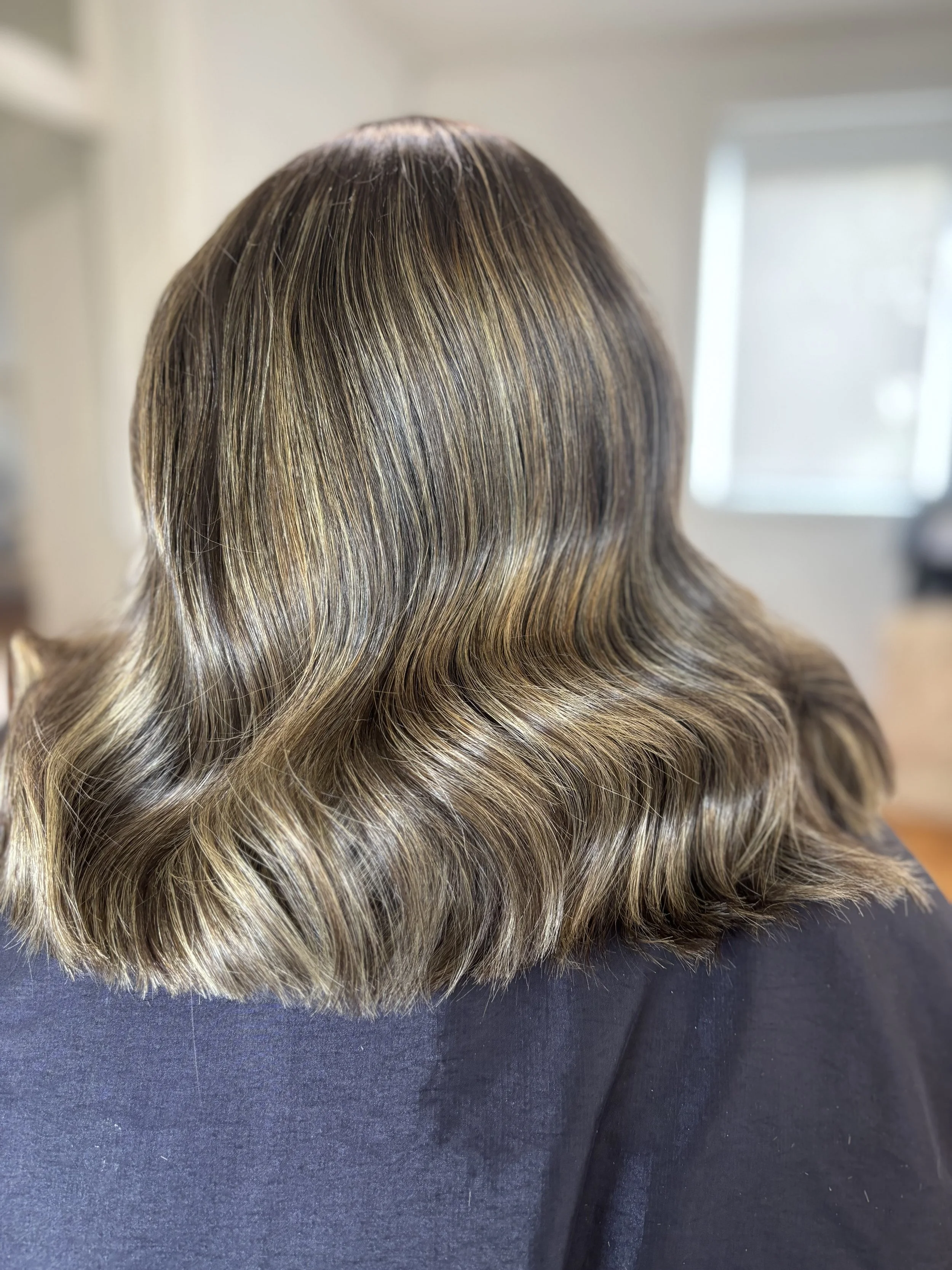 Back of a person's head showing shoulder-length wavy hair with highlights.