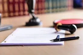 Close-up of a desk with an open notebook, a black pen, and a pink case on a blurred background.