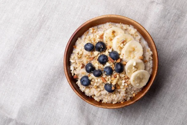A bowl of oatmeal topped with blueberries, sliced bananas, and nuts on a light-colored tablecloth.