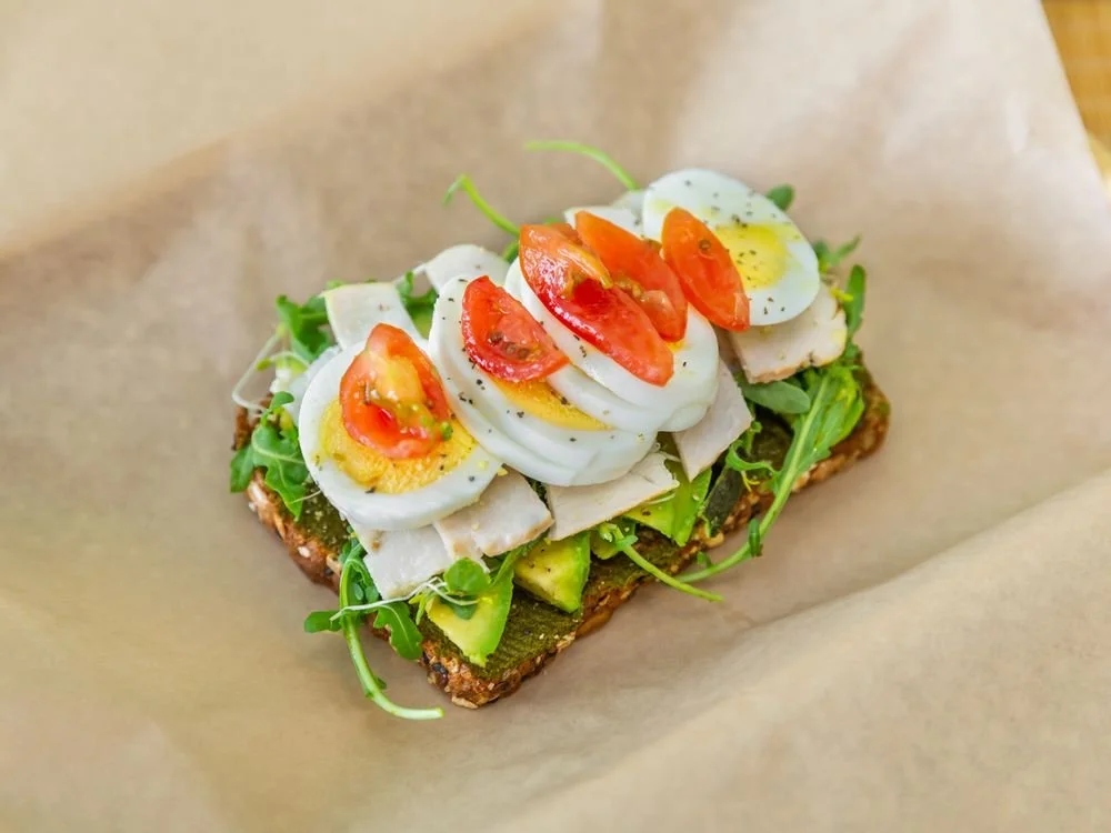 open-faced sandwich with sliced hard-boiled eggs, cherry tomatoes, avocado, greens, on whole grain toast