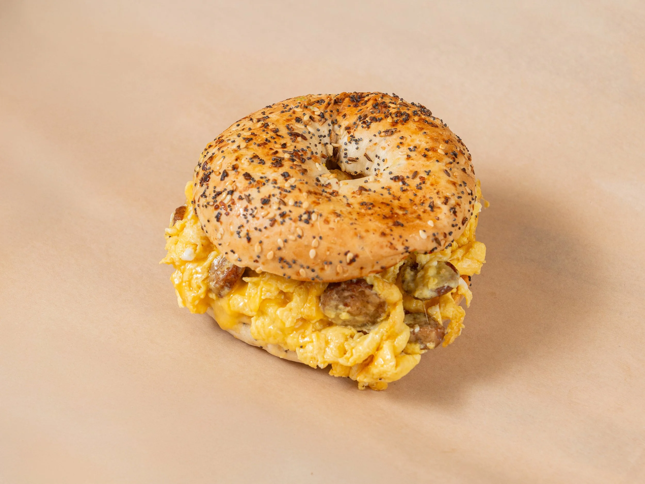Bagel sandwich with scrambled eggs and sausage bits against a beige background.