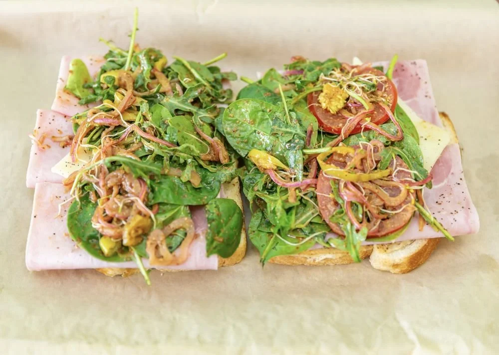 Two open-faced sandwiches with ham, fresh spinach, sliced tomato, and microgreens on toasted bread.