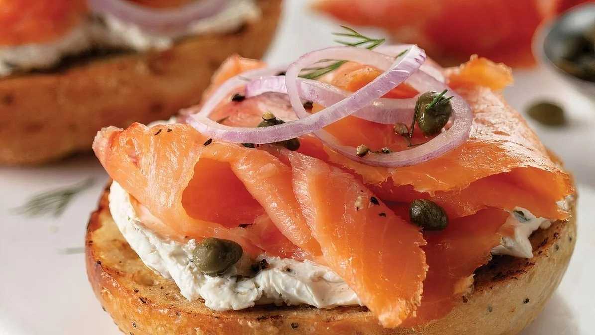 Close-up of a bite-sized bagel topped with smoked salmon, cream cheese, red onion slices, capers, and herbs.