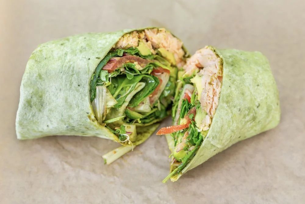 A wrap cut in half, showing lettuce, tomatoes, grilled chicken, and other vegetables inside.