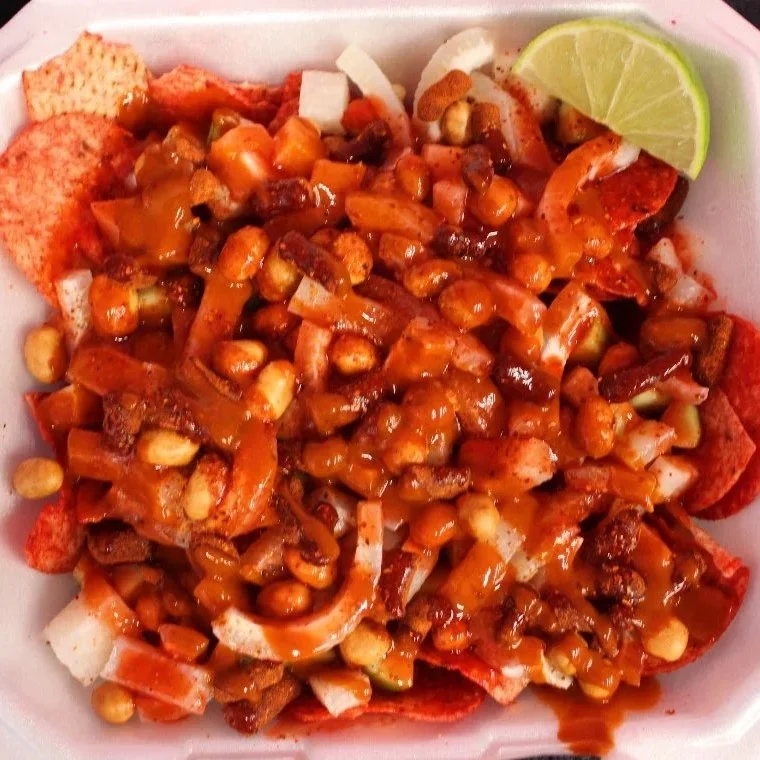 Bowl of nachos topped with shredded cheese, chili, beans, onions, and a lime wedge.