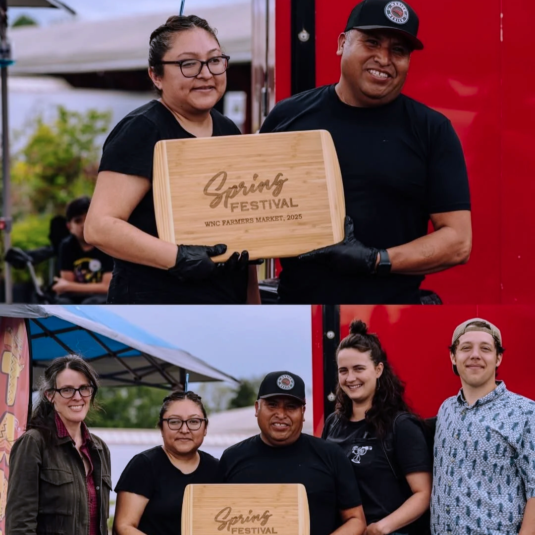 Group of people at a spring festival, some holding a wooden sign that says "Spring Festival WNC Farmers Market, 2025".