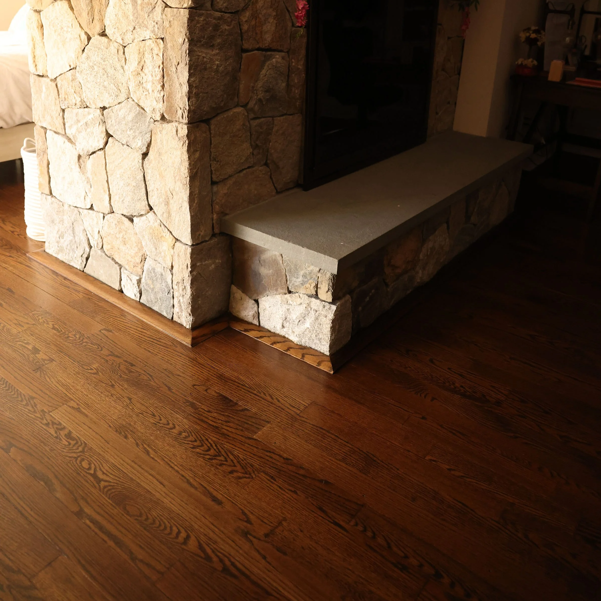 Corner of a stone fireplace with a wooden floor and built-in hearth.