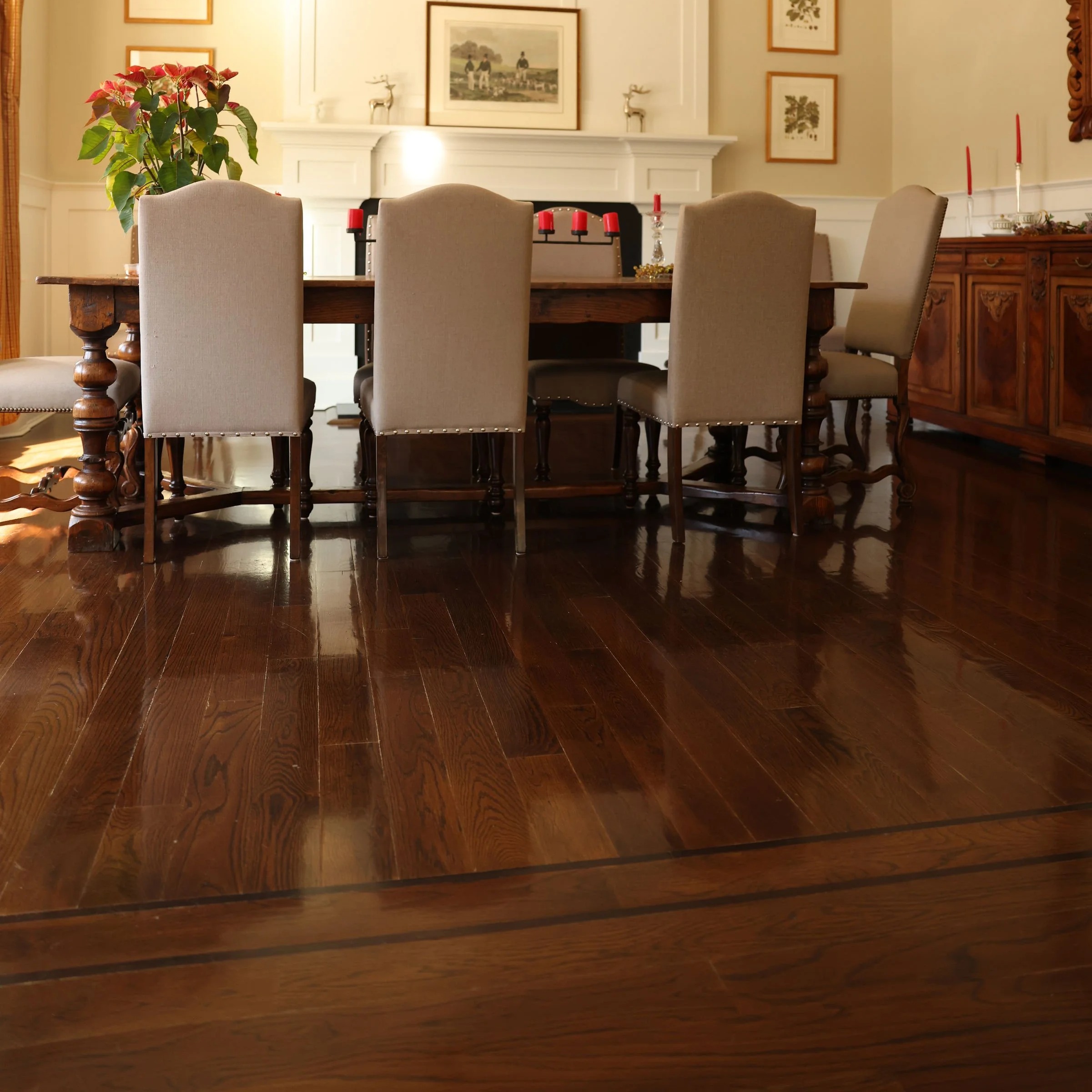 A dining room with a dark wood table, cream upholstered chairs, and a sideboard, decorated with candles, a poinsettia plant, and framed pictures on the wall.