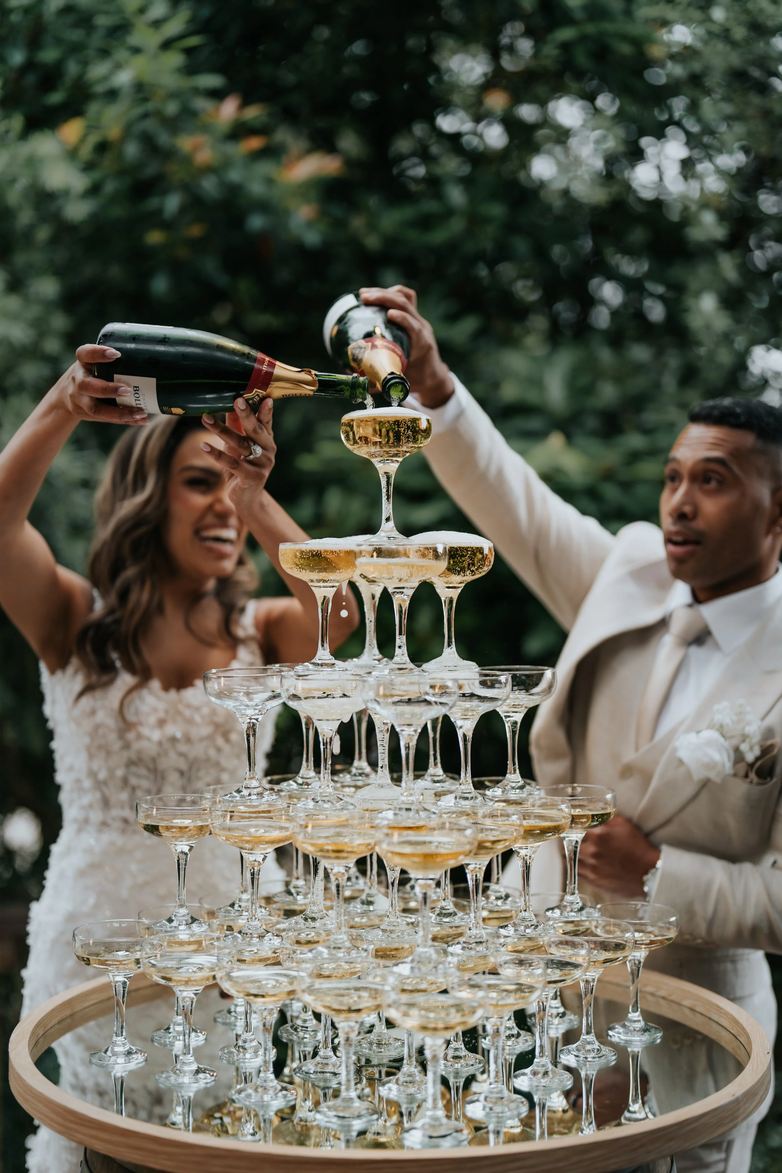 A bride and groom pouring champagne into a tower of glasses at their wedding reception.