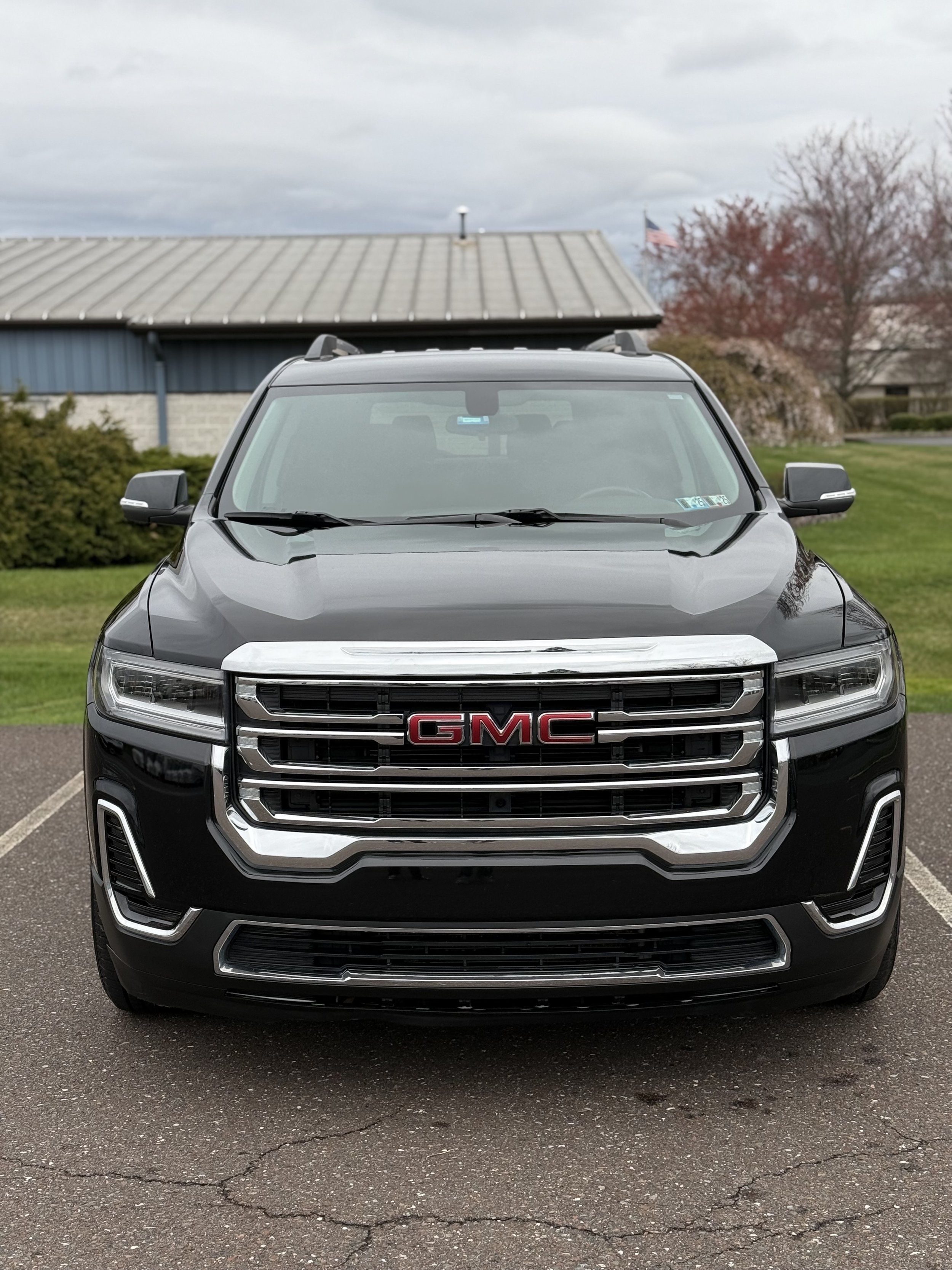 Front view of a black GMC SUV parked on a paved lot with a building and trees in the background.