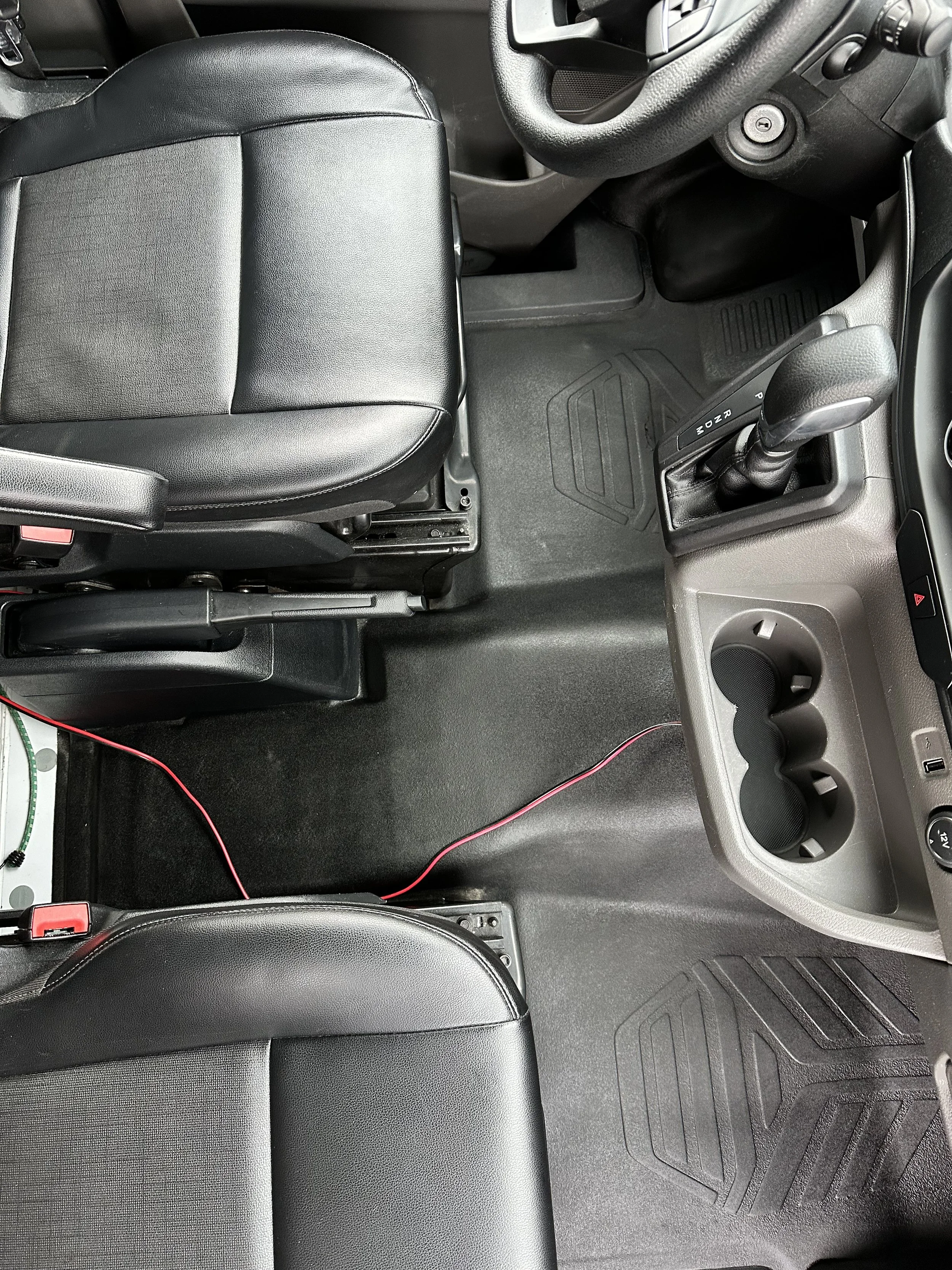 Interior of a vehicle showing the driver and passenger seats, gear shift, steering wheel, and cup holders.