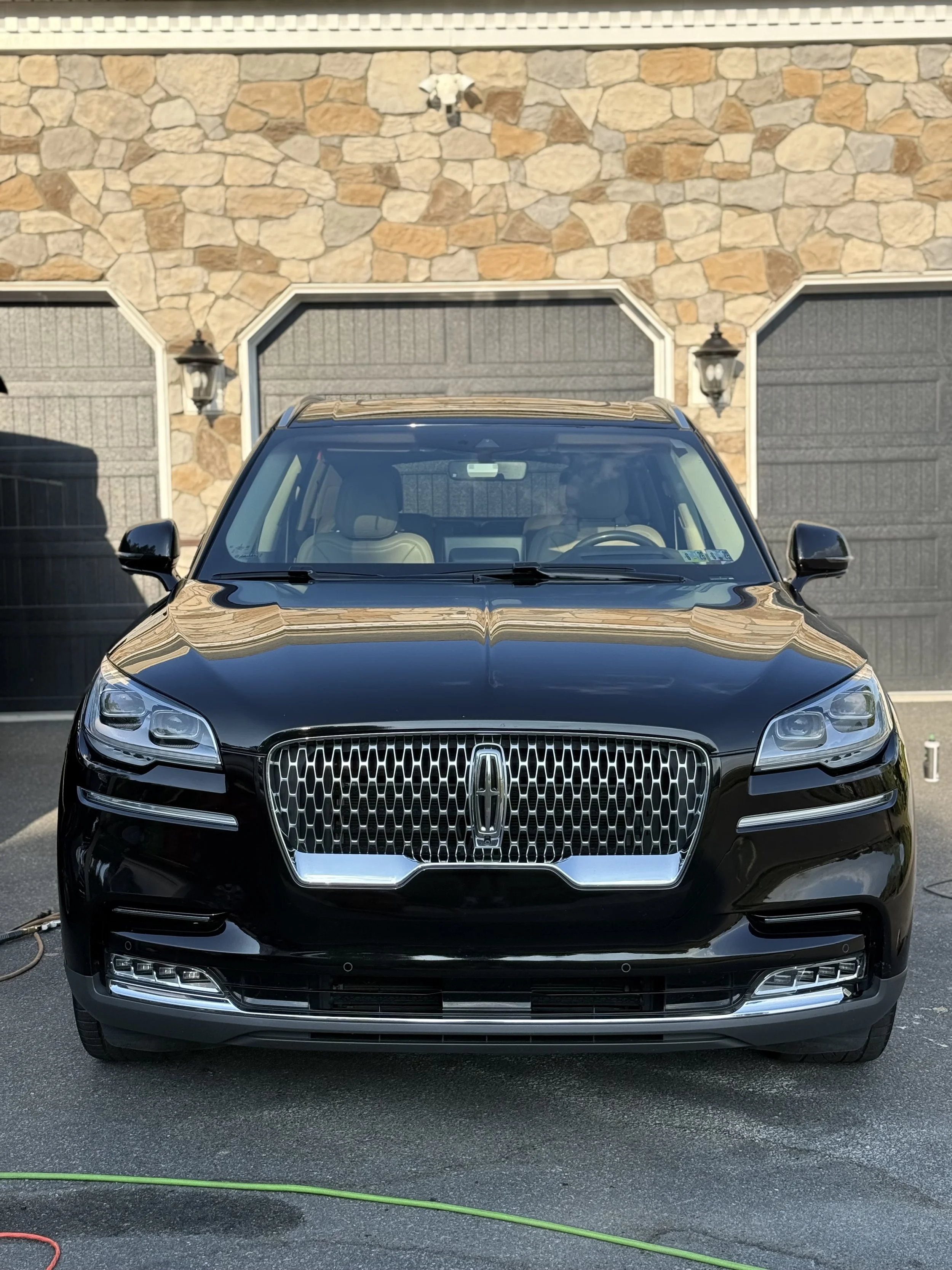 Front view of a parked black Lincoln SUV with a stone wall and two garage doors in the background.