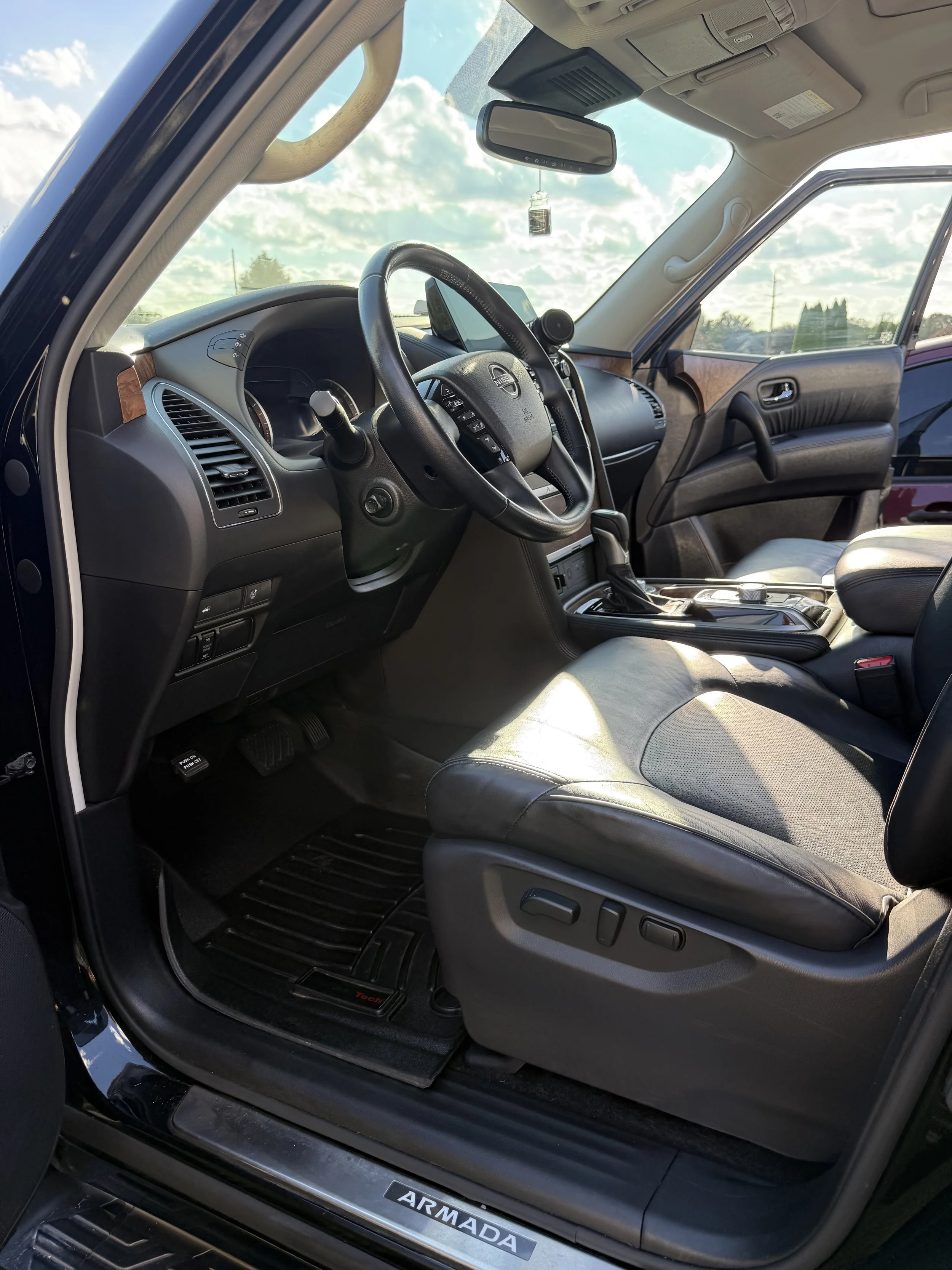 The interior of a black Toyota Armada SUV, showing the driver's seat, steering wheel, dashboard, and part of the passenger seat, with a view of the sky through the windshield.