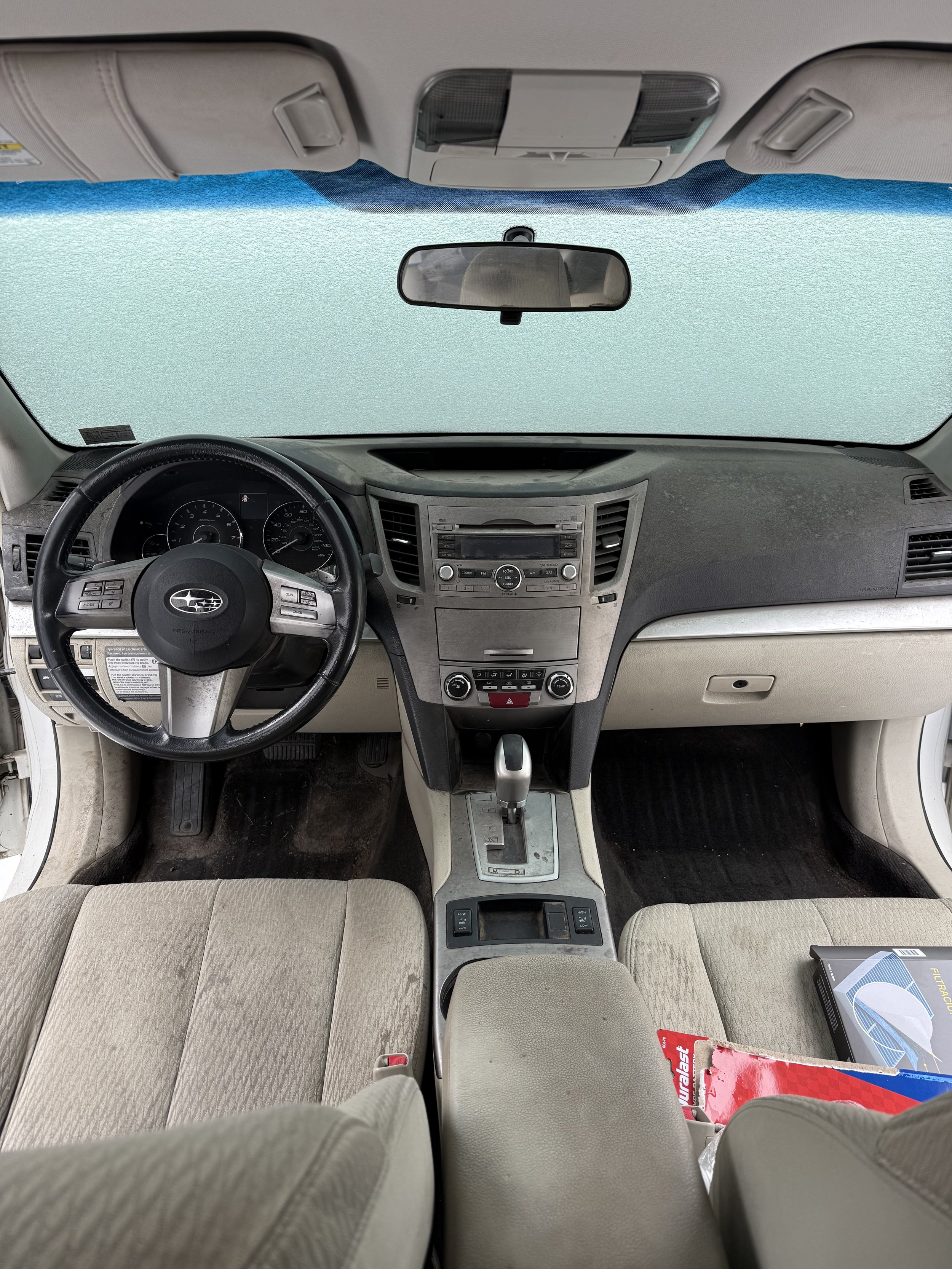 Interior view of a vehicle dashboard showing the steering wheel, rearview mirror, windshield, seats, and center console with gear shifter.