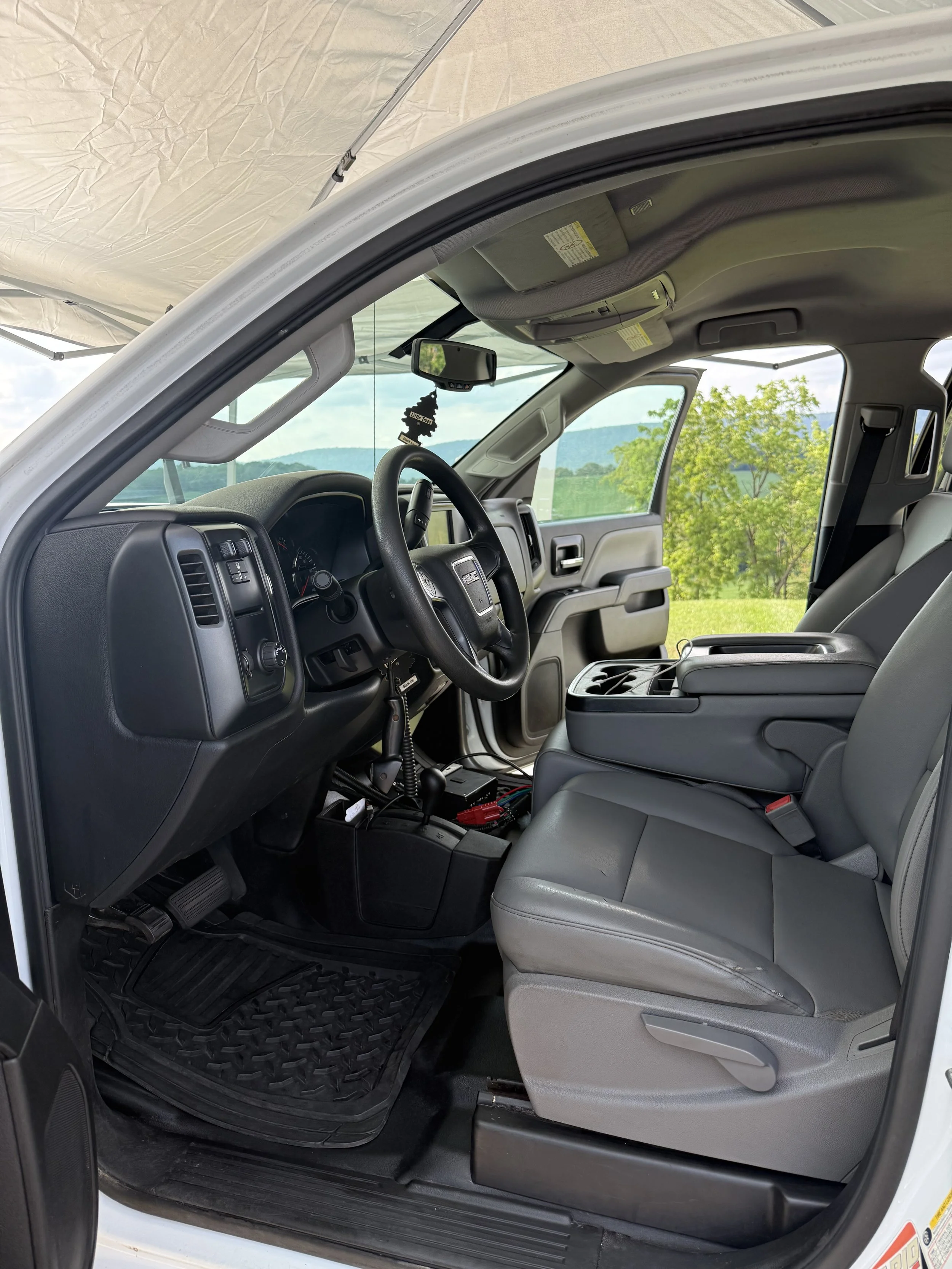 Interior of a vehicle, showing the driver's seat, dashboard, steering wheel, and front passenger seat with outdoor scenery visible through the windows.