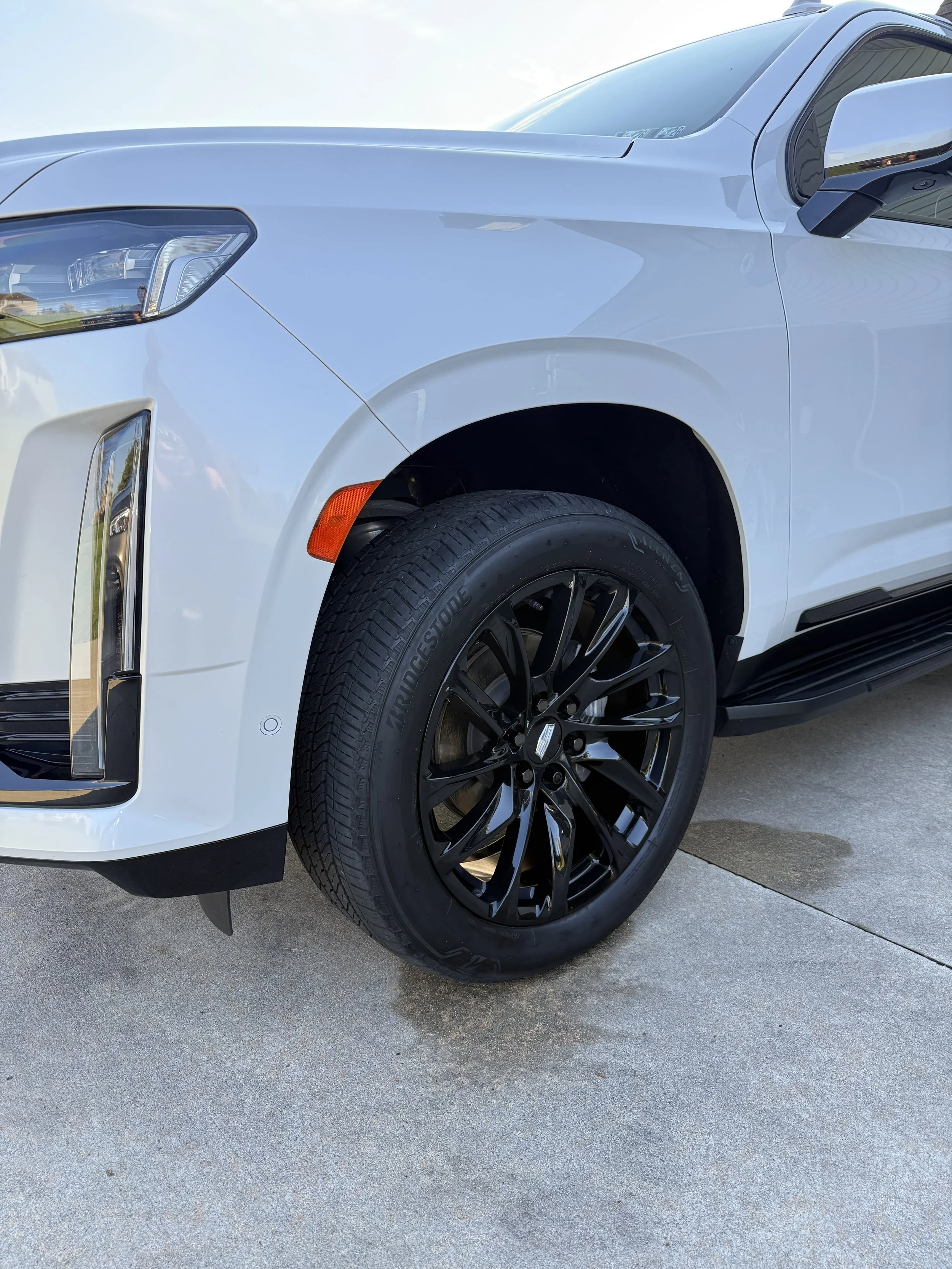 Close-up of the front right section of a white SUV, showing black wheels, tire, headlight, and a side mirror.