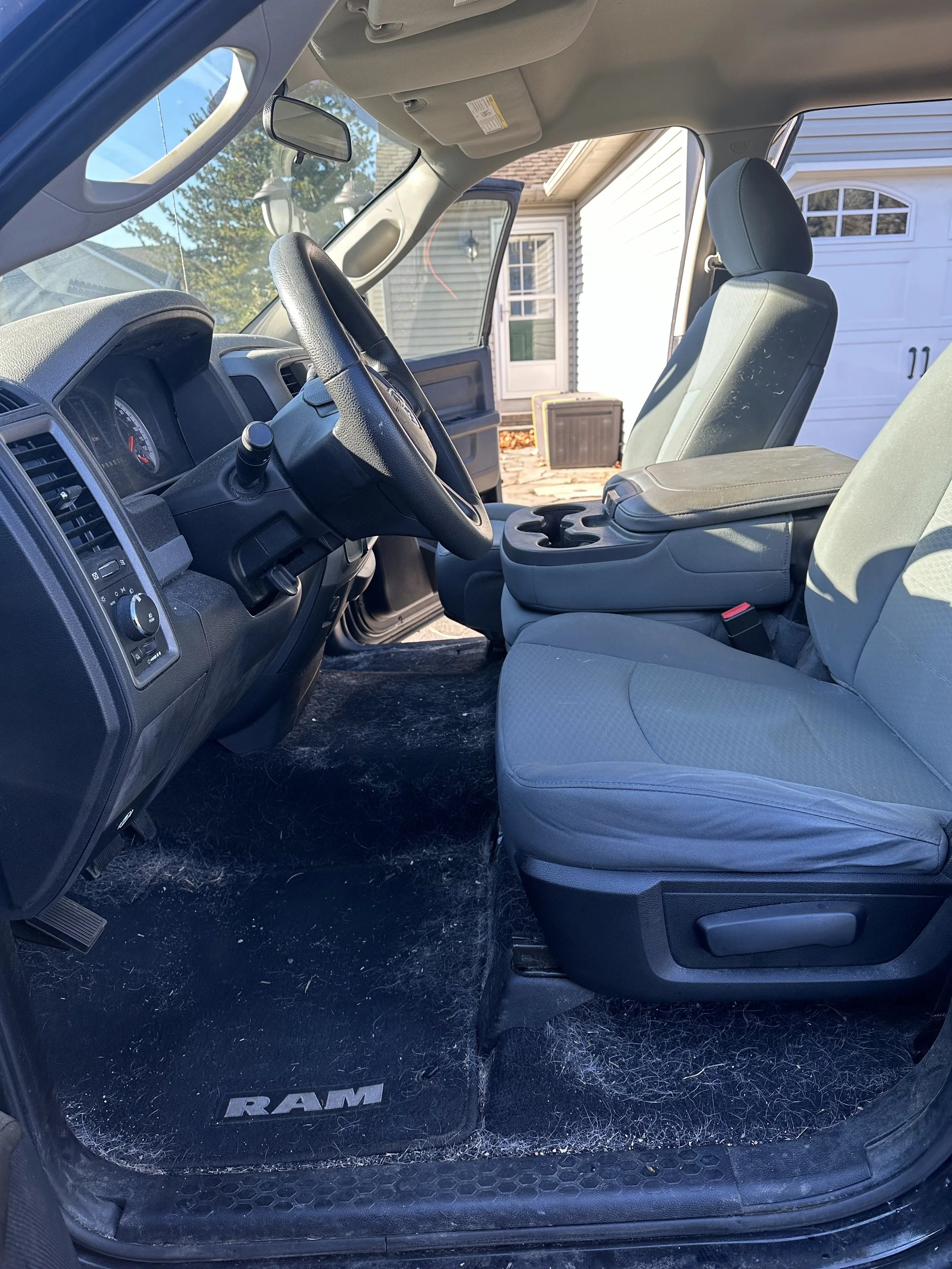 Interior of a Ram truck, showing the front seats, dashboard, steering wheel, and center console with cup holders. The floor is dirty with dust and debris.