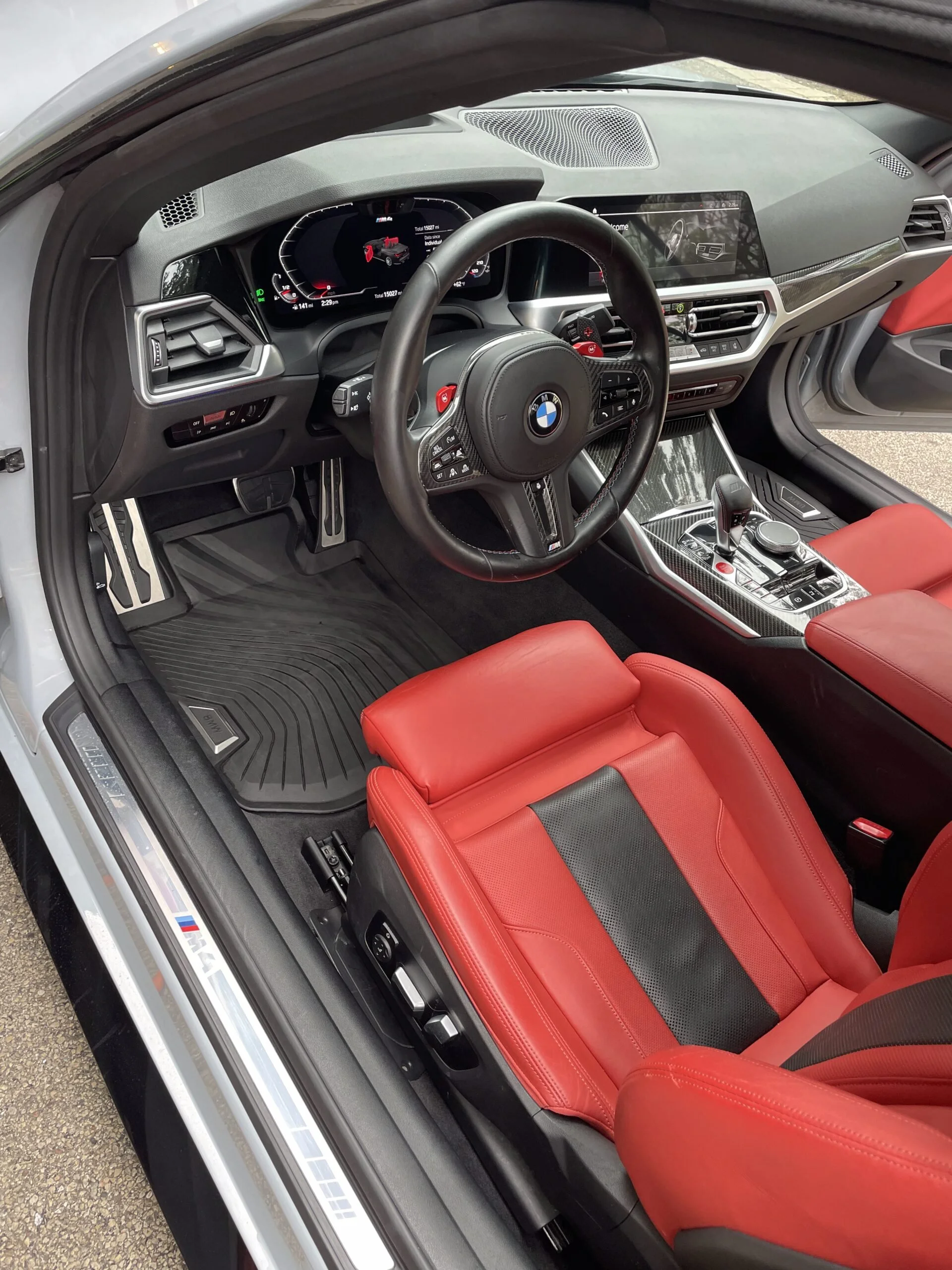 The interior of a modern BMW sports car featuring a digital dashboard, a multifunction steering wheel, a central control display, and red leather seats.