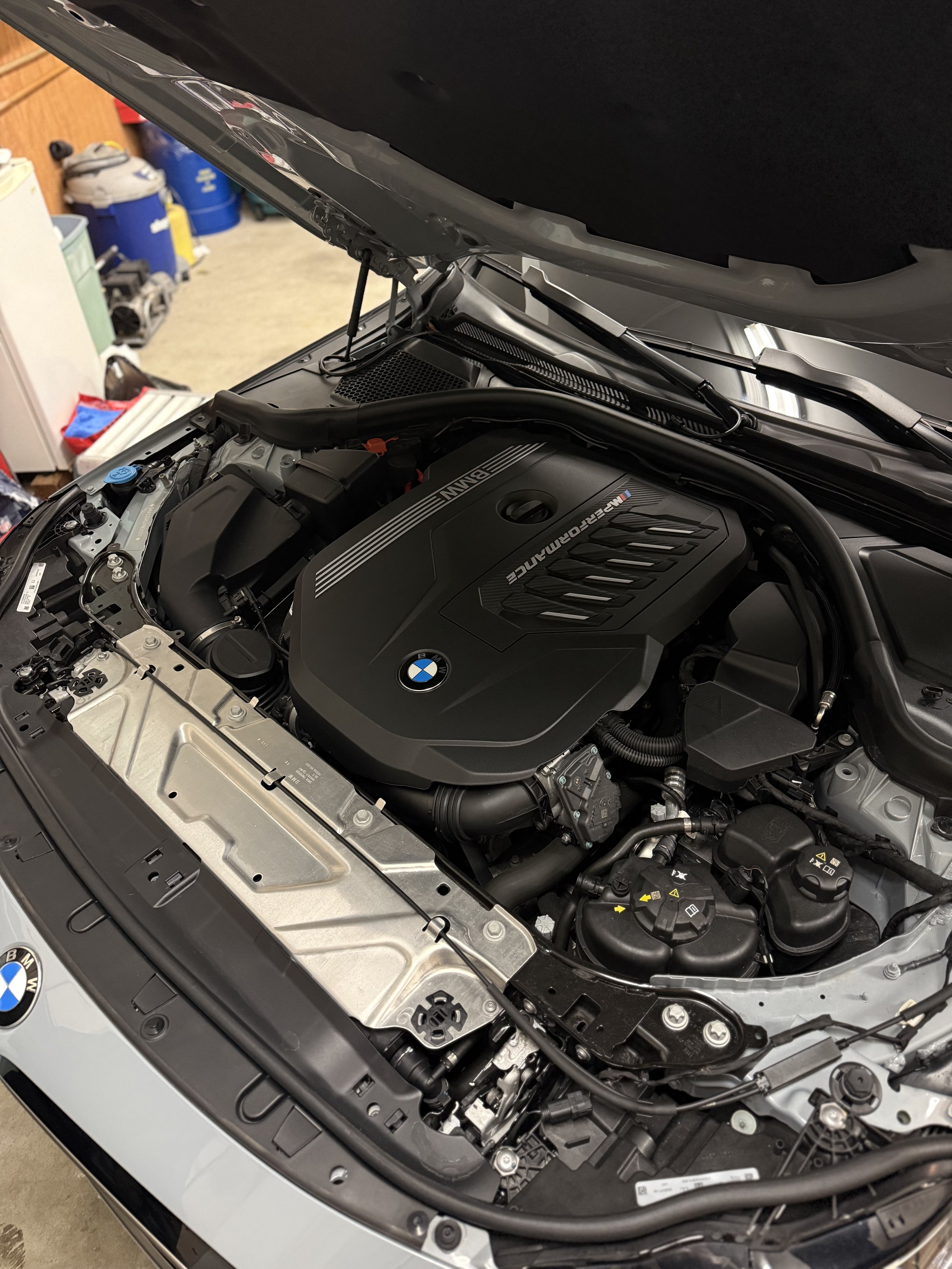 Close-up view of a clean BMW engine in a car with the hood open inside a garage.