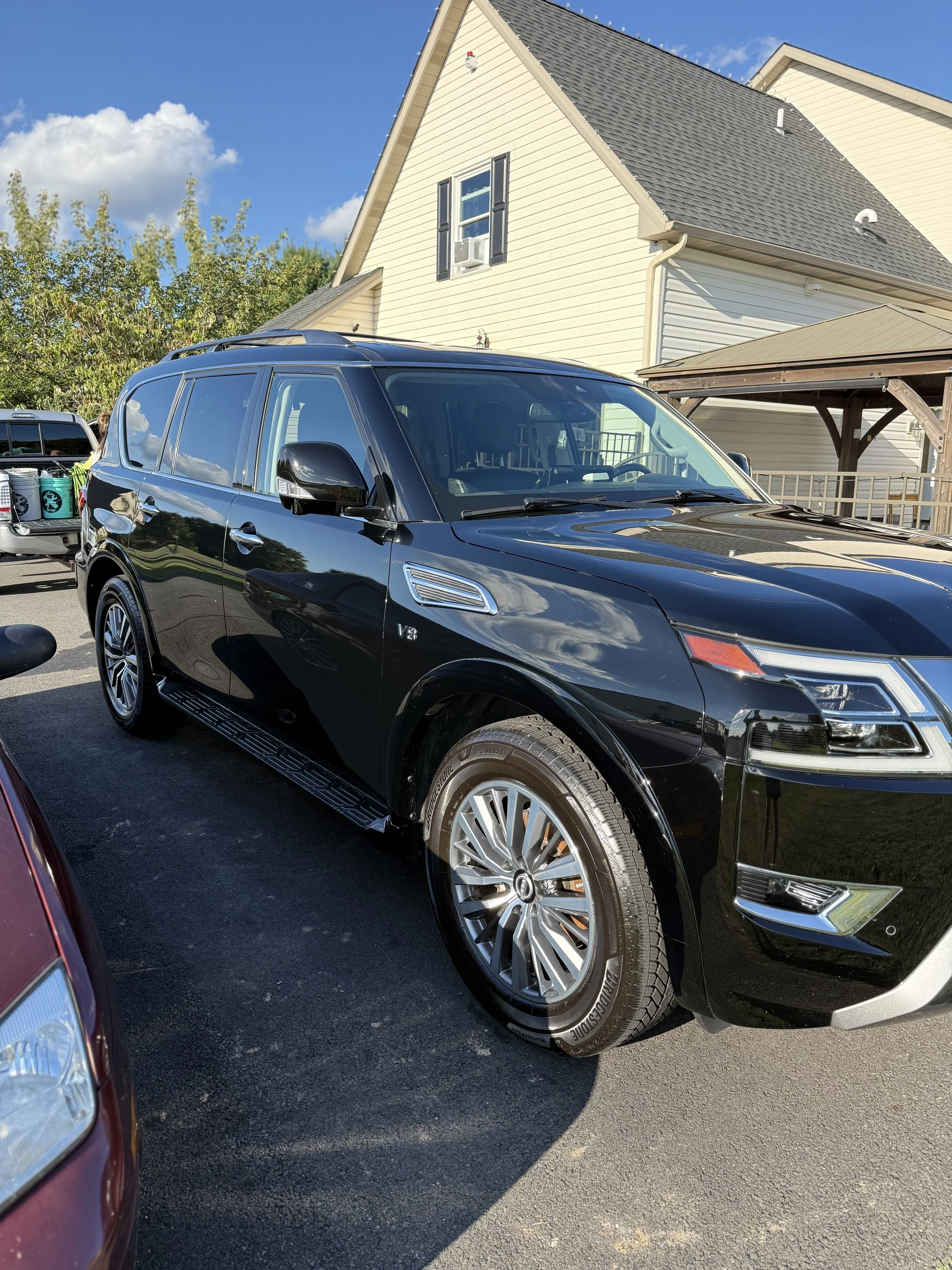 A black luxury SUV parked on a residential driveway with a beige house and blue sky in the background.