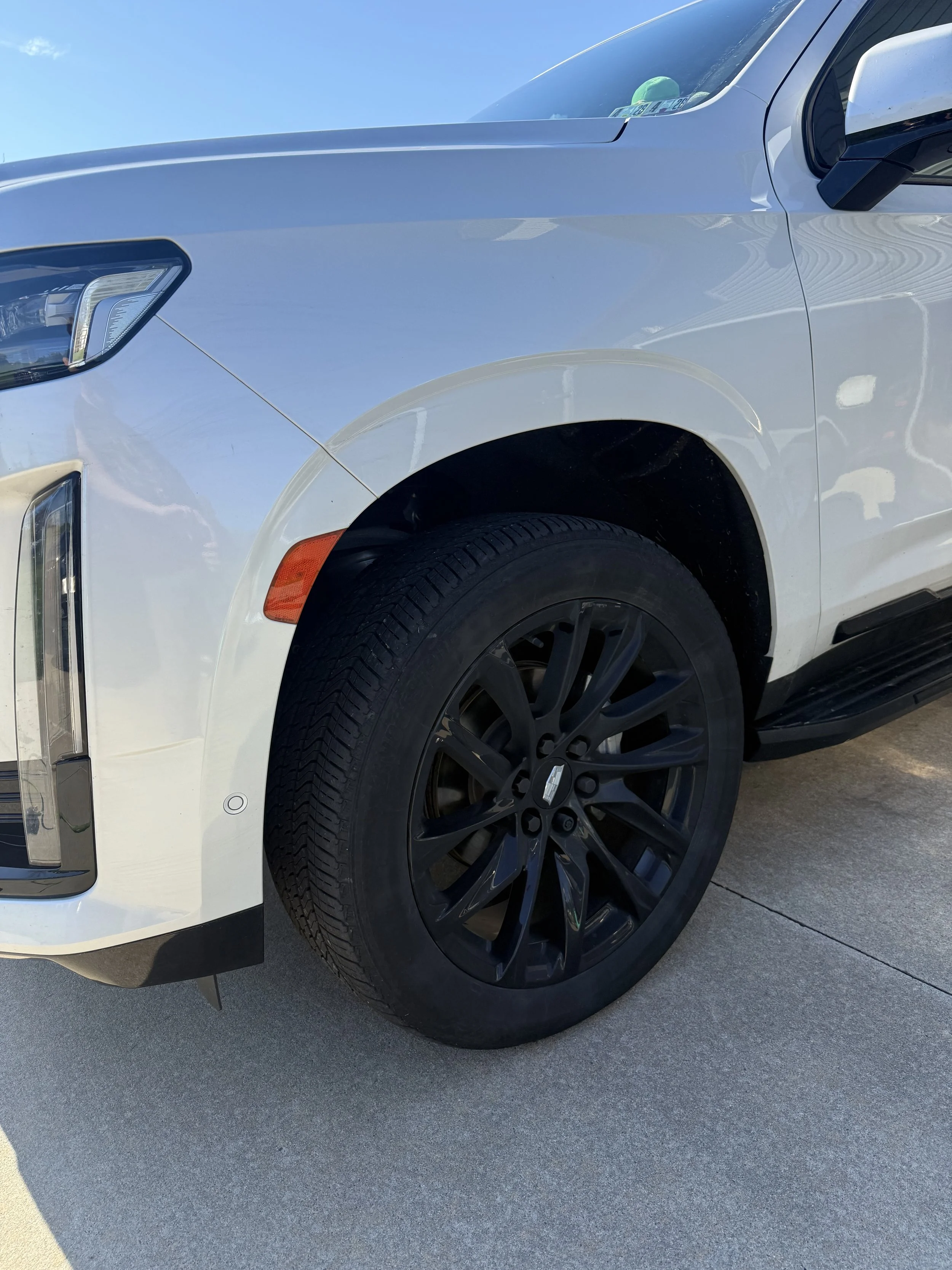 Close-up of a white SUV front wheel with black rim parked on concrete ground.