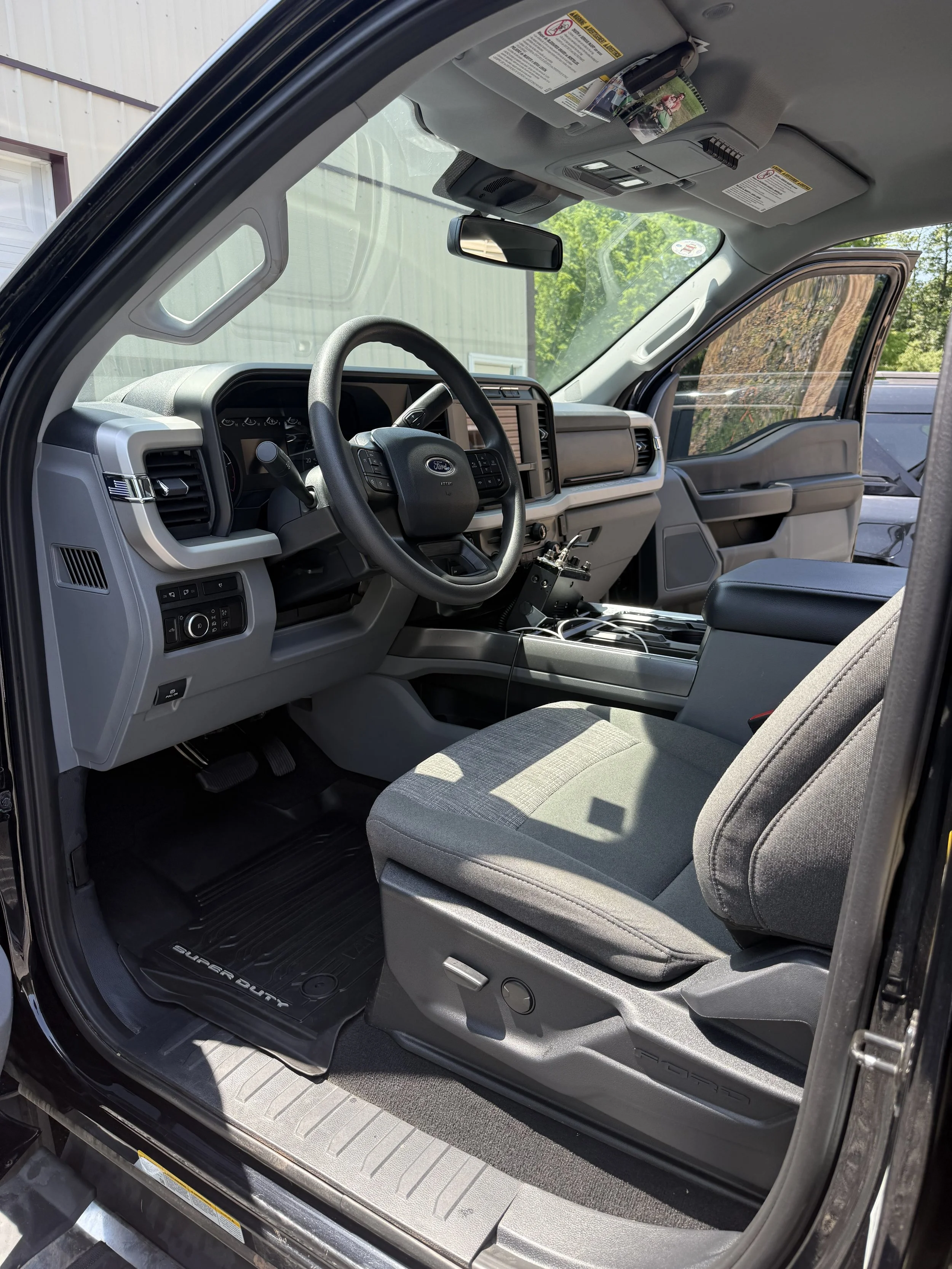 Interior of a Ford Super Duty truck, showing the driver's seat, steering wheel, dashboard, and center console with electronic equipment, with sunlight coming through the window.