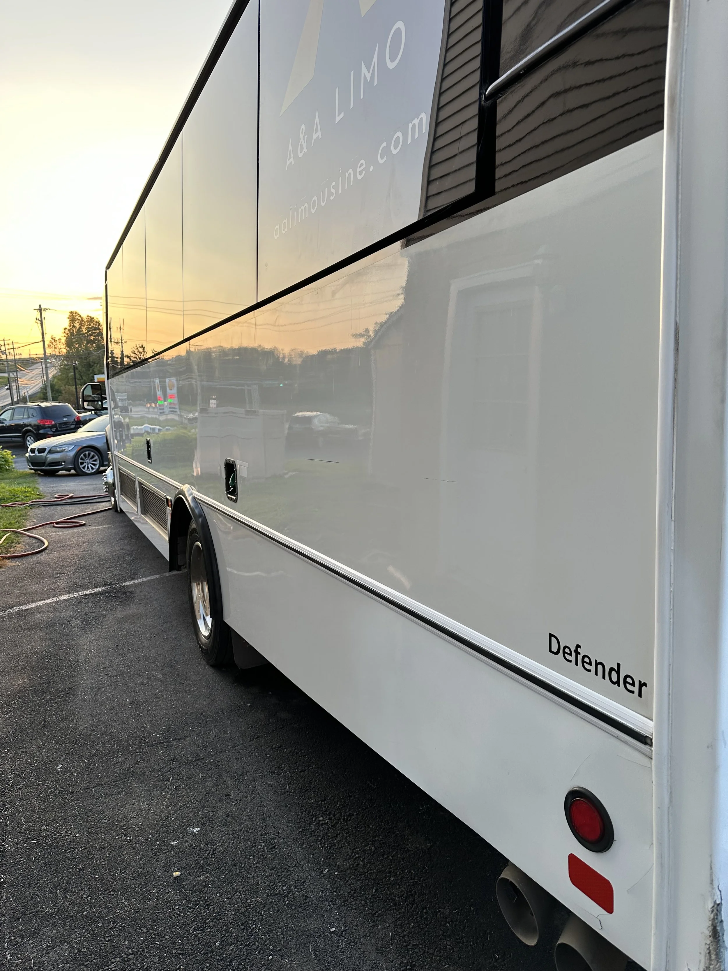 White mobile food or service truck with the label 'Defender' on the lower right corner, parked on asphalt during sunset, with other parked cars and power lines in the background.