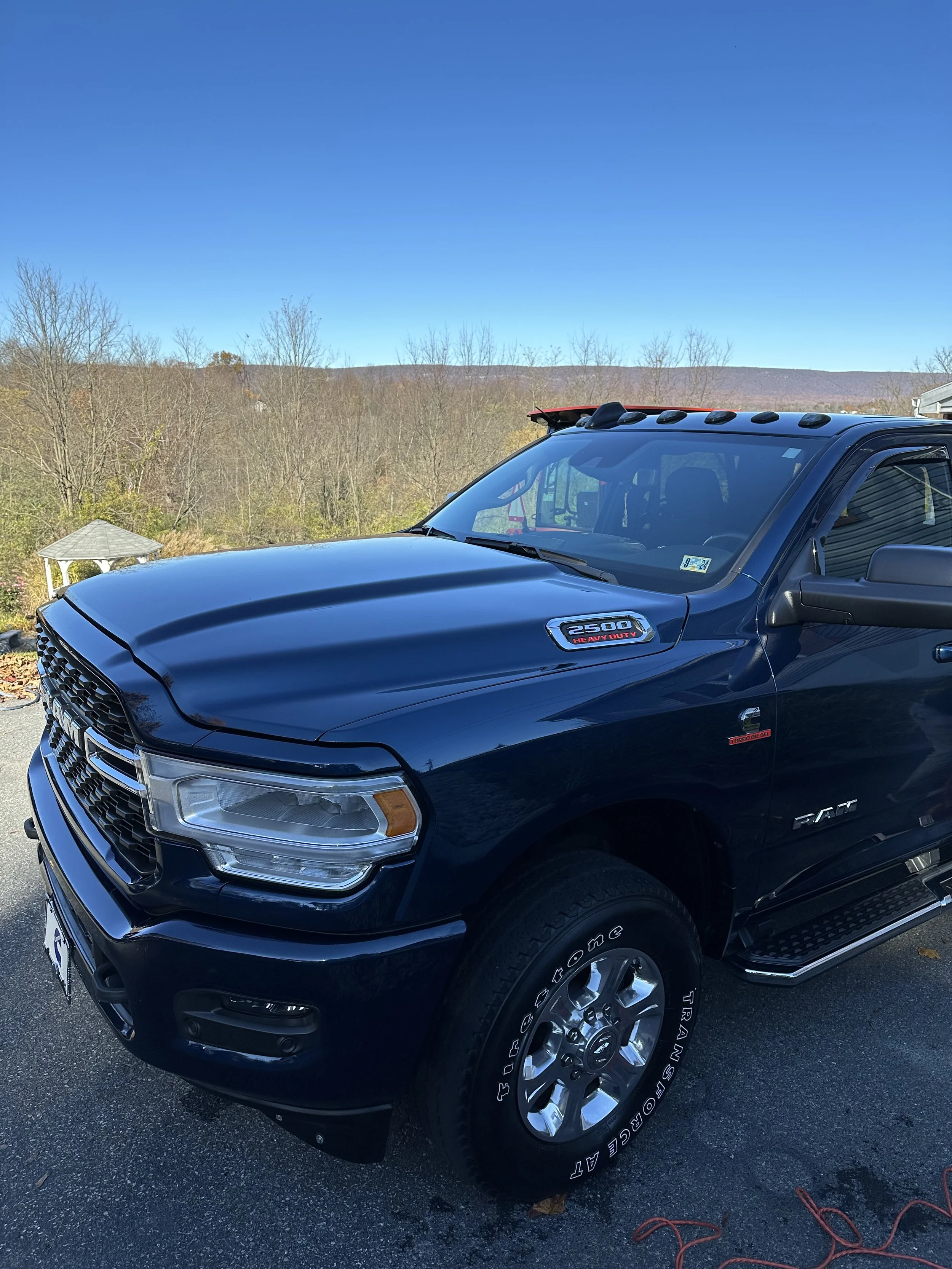 Black RAM 2500 heavy-duty pickup truck parked outdoors with a clear blue sky and leafless trees in the background.