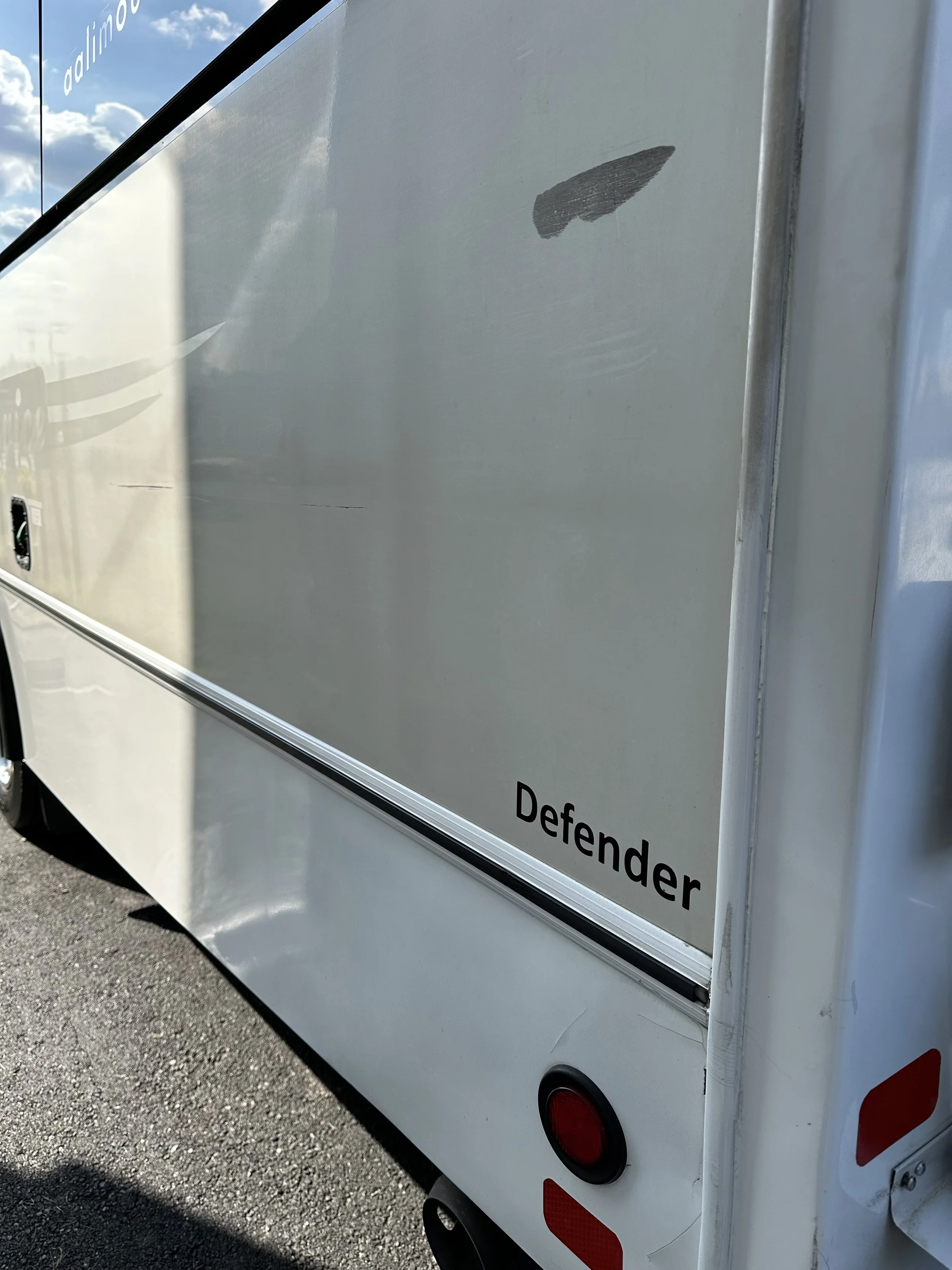 Close-up of the side of a white vehicle, with the word 'Defender' written on it, and a small black bird-shaped decal near the top.
