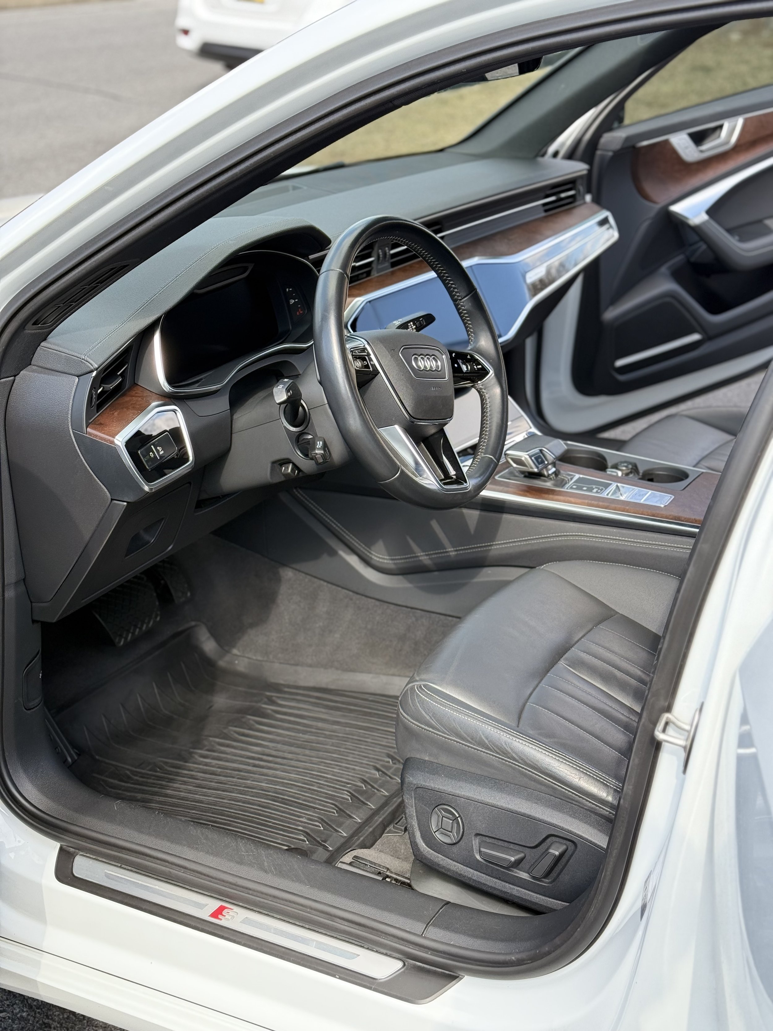 Interior of a modern Audi car showing the driver's seat, steering wheel, dashboard, gear shift, and center console with wood trim.