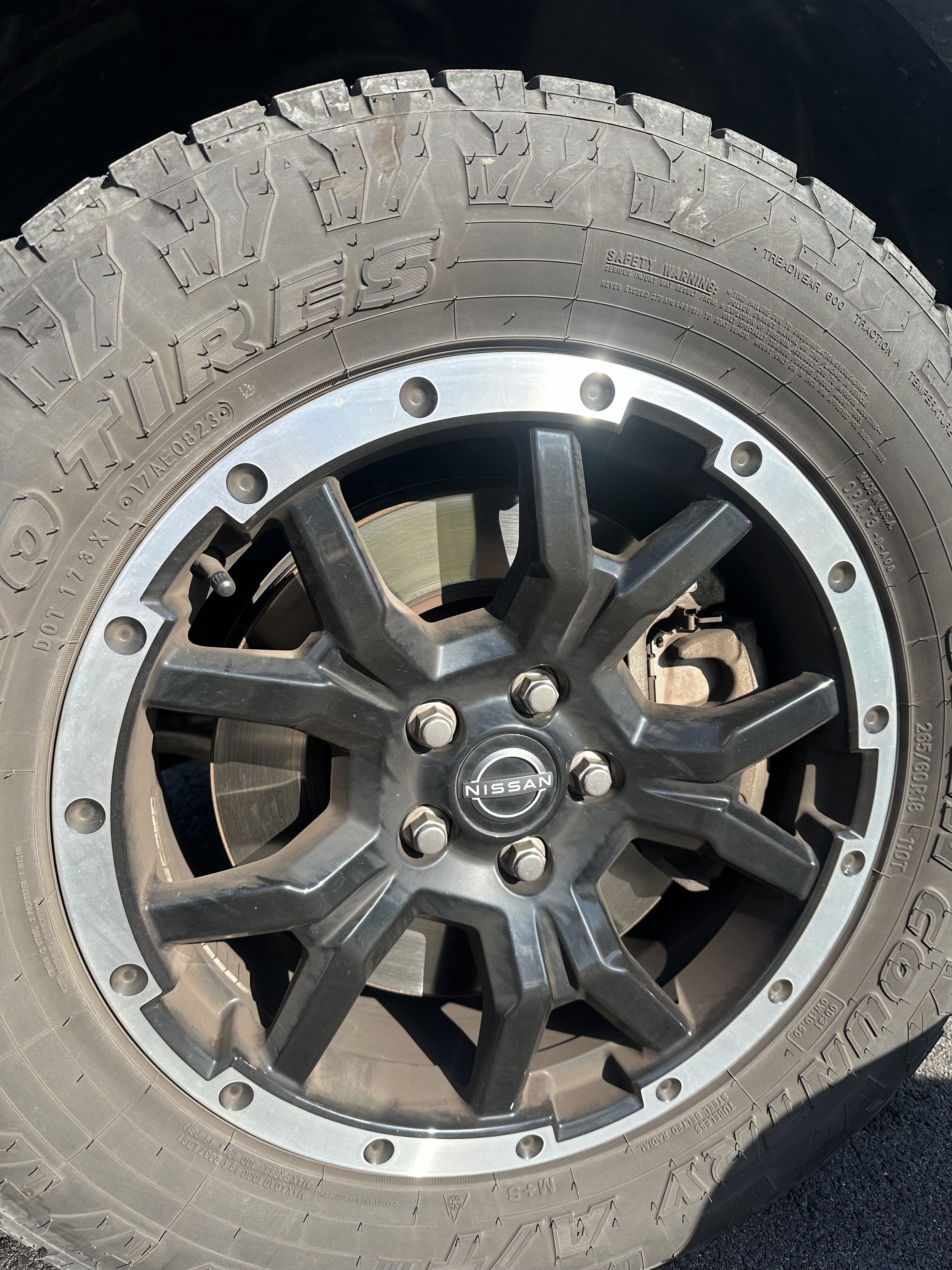 Close-up of a Nissan vehicle alloy wheel and tire, showing the Nissan logo at the center of the wheel and the tread pattern on the tire.
