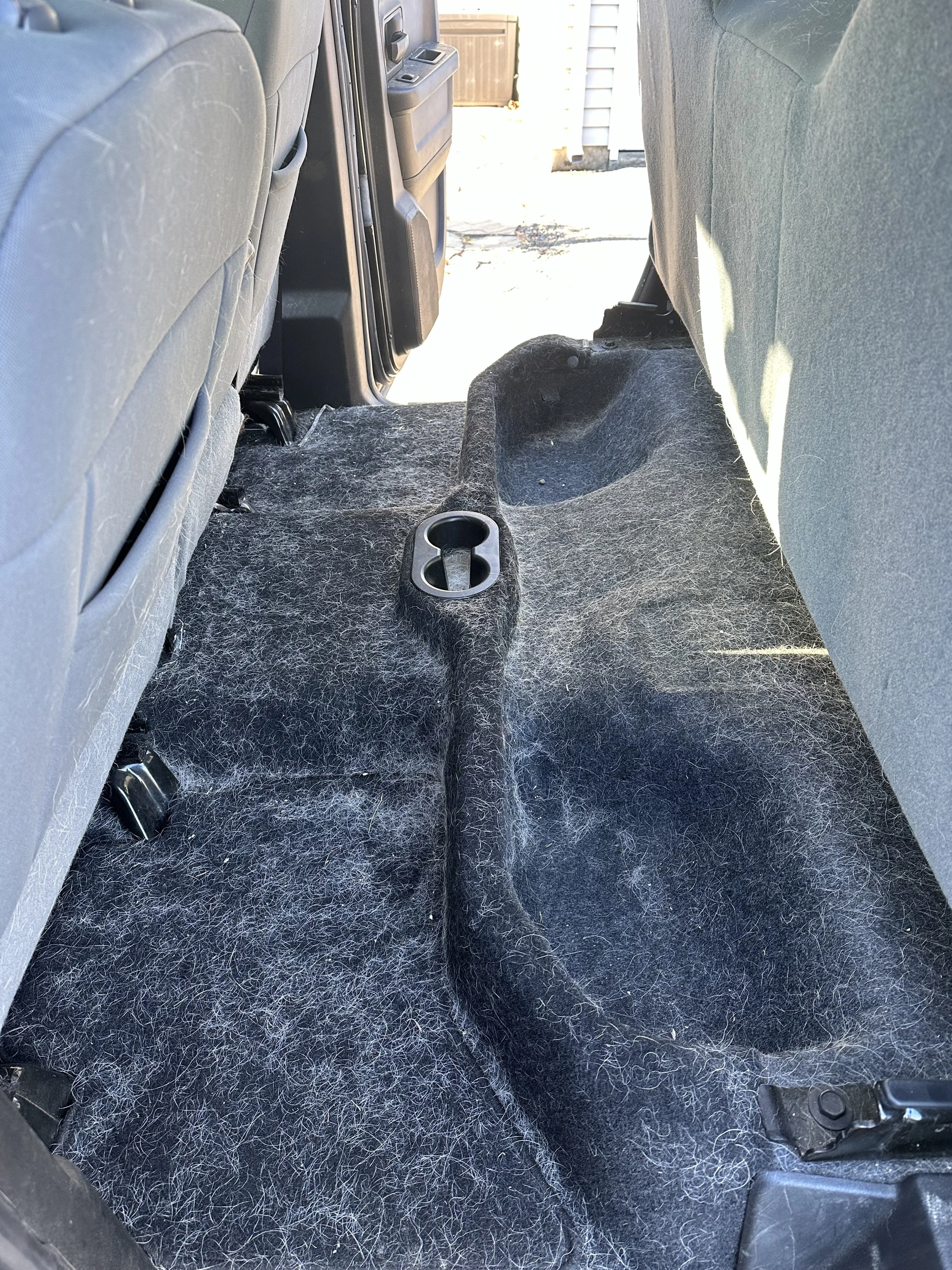 Backseat interior of a car showing a black carpeted floor with visible hair and a plastic cup holder.
