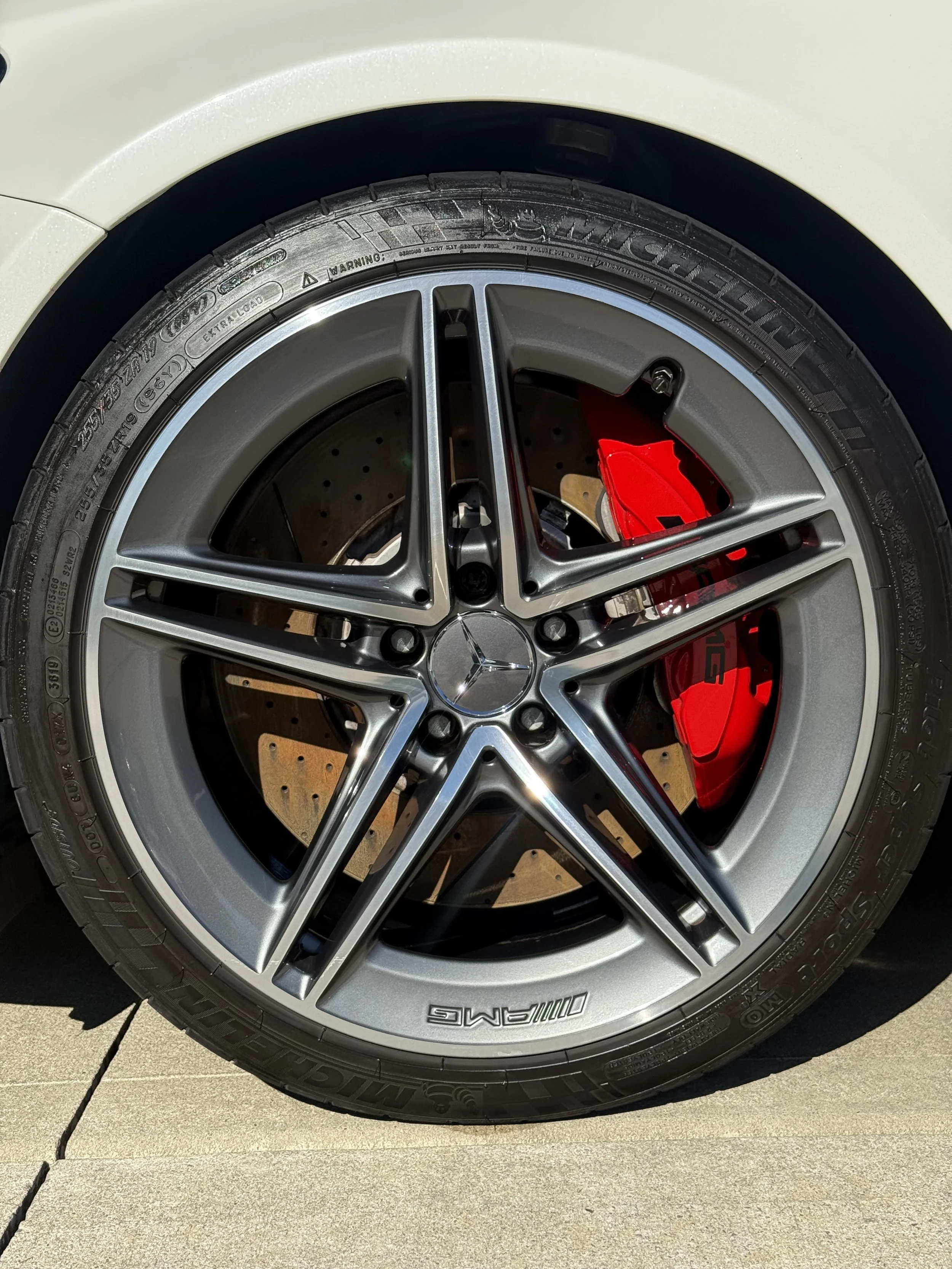 Close-up of a Mercedes-Benz car wheel with a silver alloy rim, a Michelin tire, and a red brake caliper visible in the background.