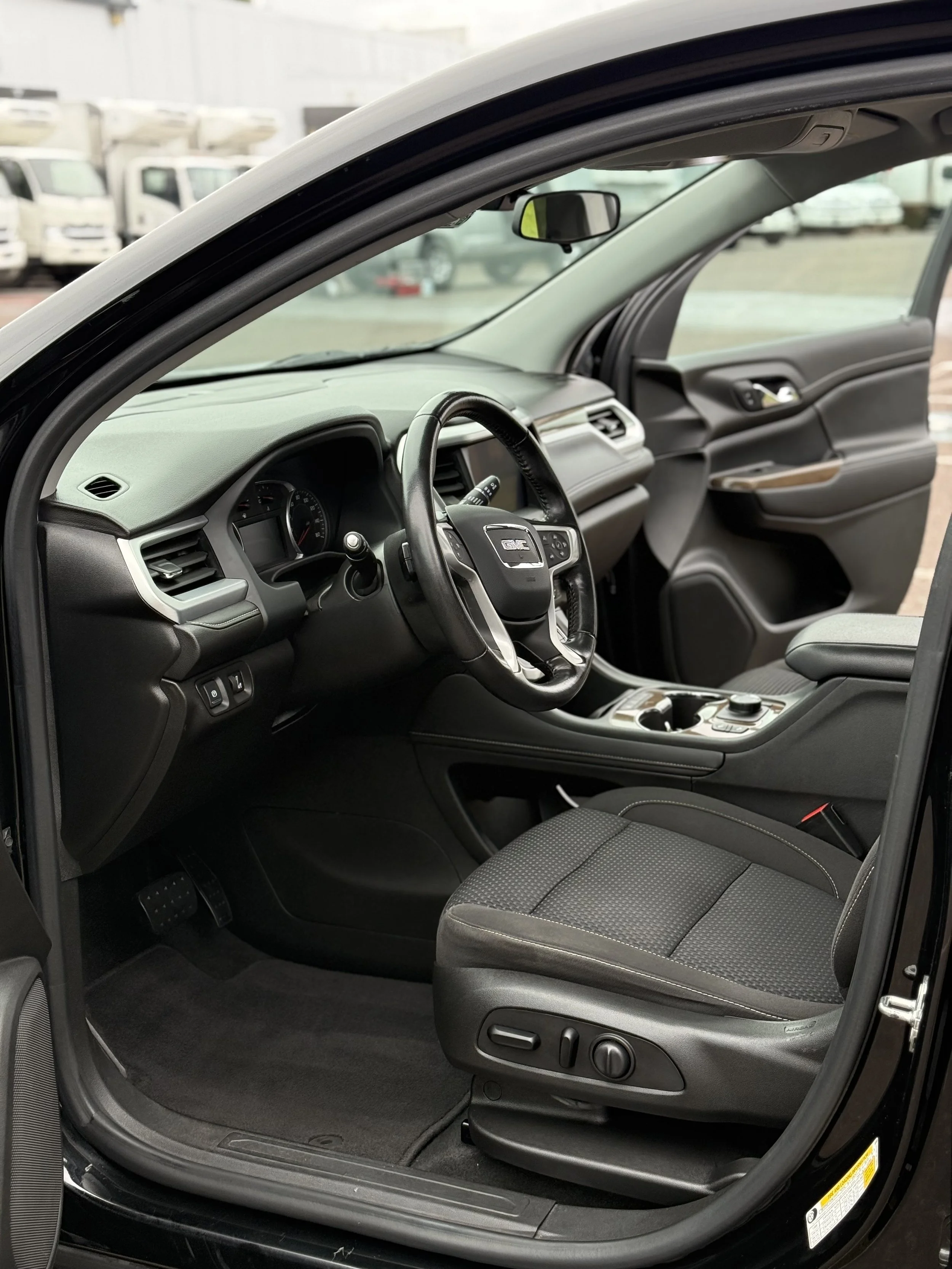 Interior of a black vehicle, showing the driver's seat, steering wheel, dashboard, and front passenger seat with visible controls and buttons.
