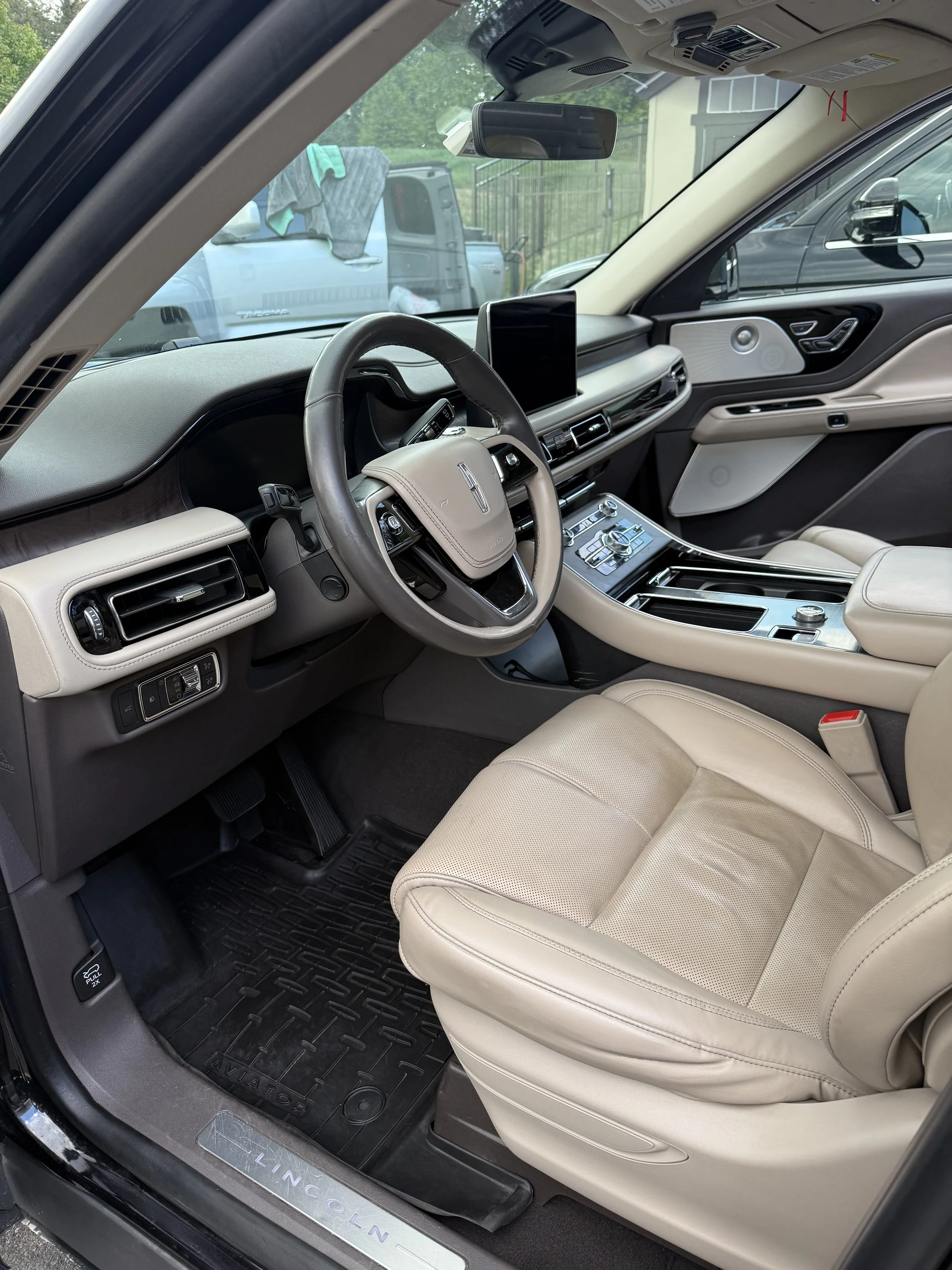 Interior of a Lincoln vehicle showing a beige leather seat, steering wheel, dashboard, center console, and a digital display screen.