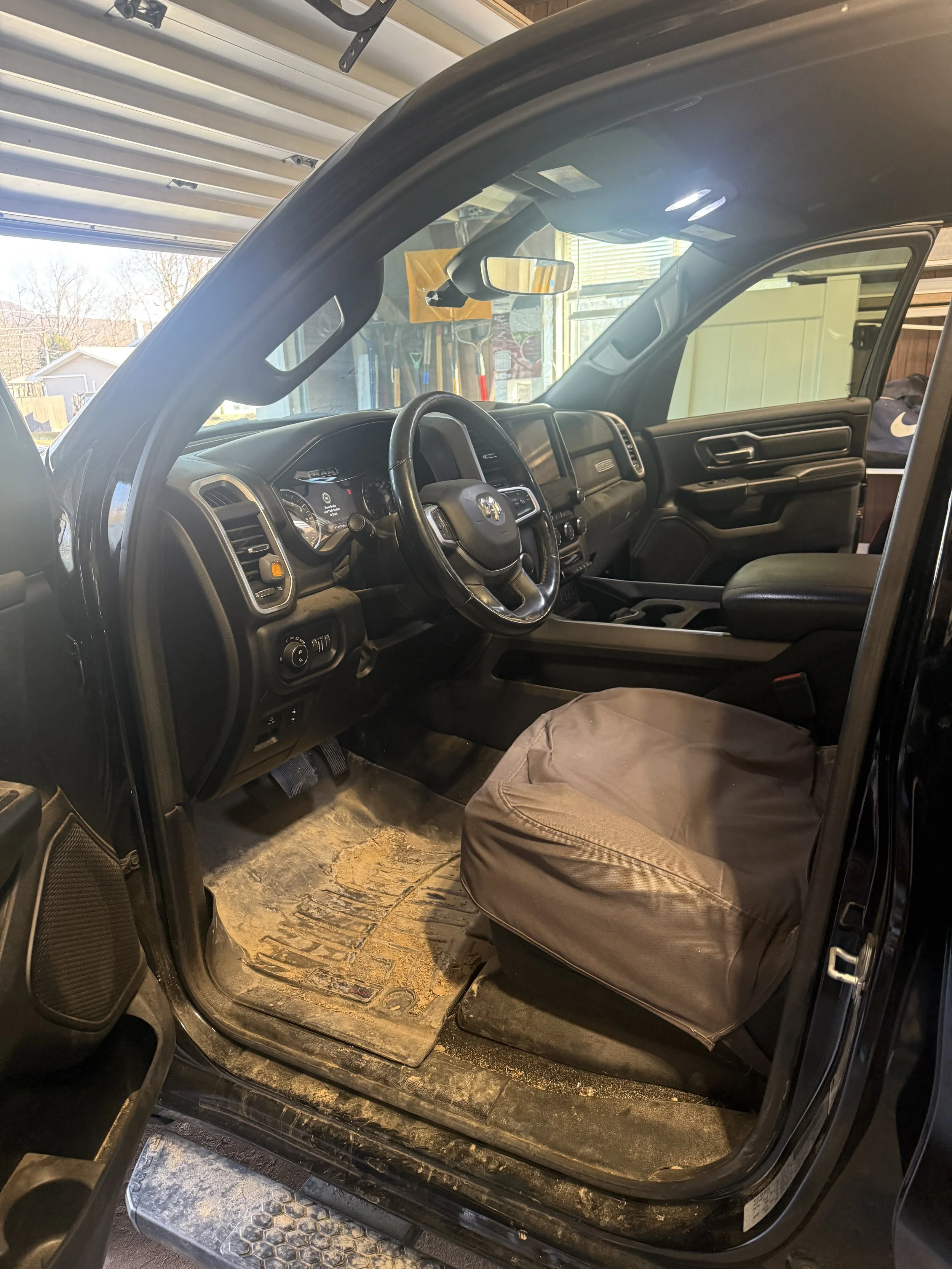 The interior of a pickup truck showing the driver's seat, steering wheel, dashboard, and a muddy floor mat.