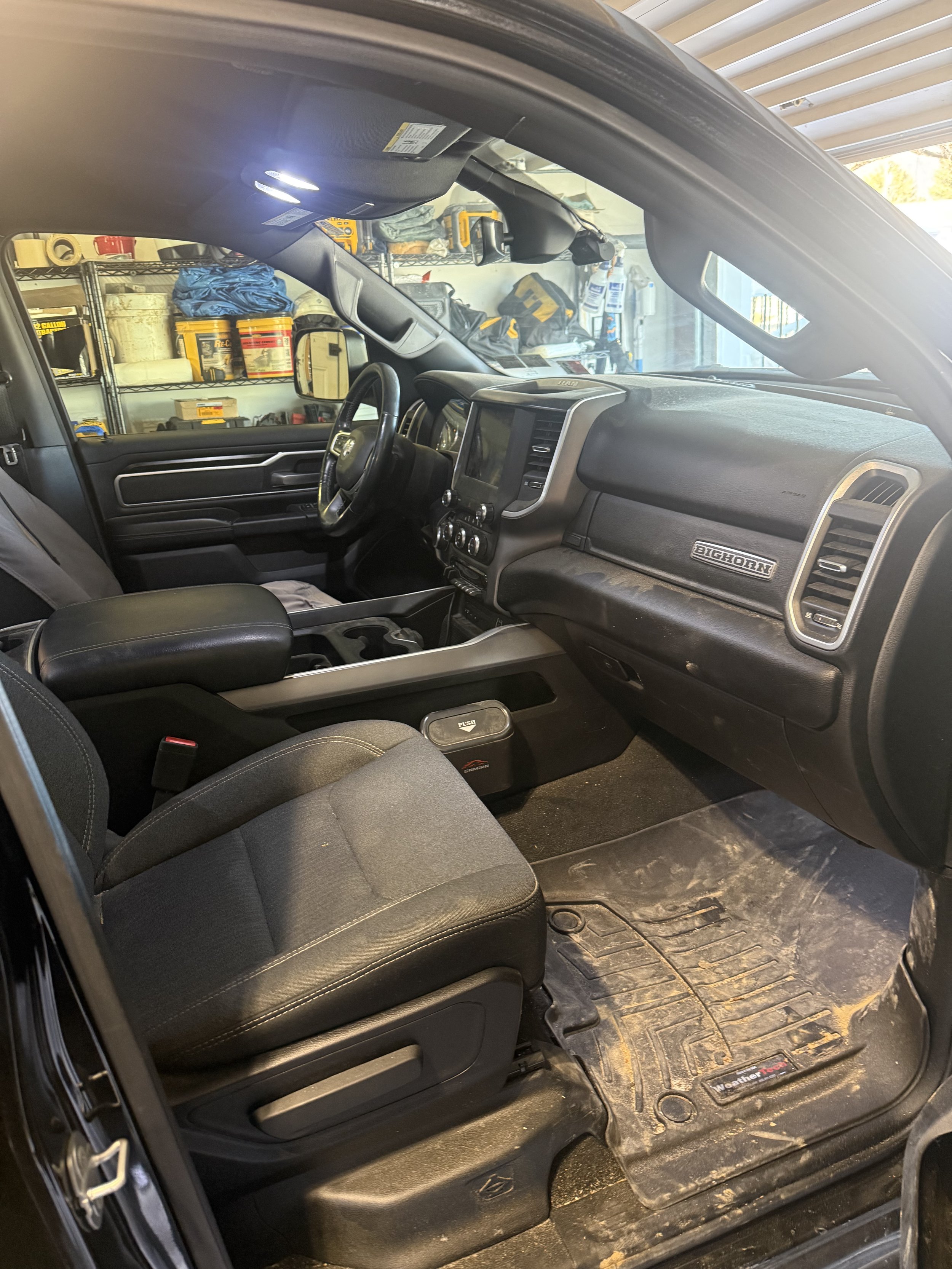 Interior of a pickup truck showing driver's seat, dashboard, and garage in the background with tools and supplies on shelves.