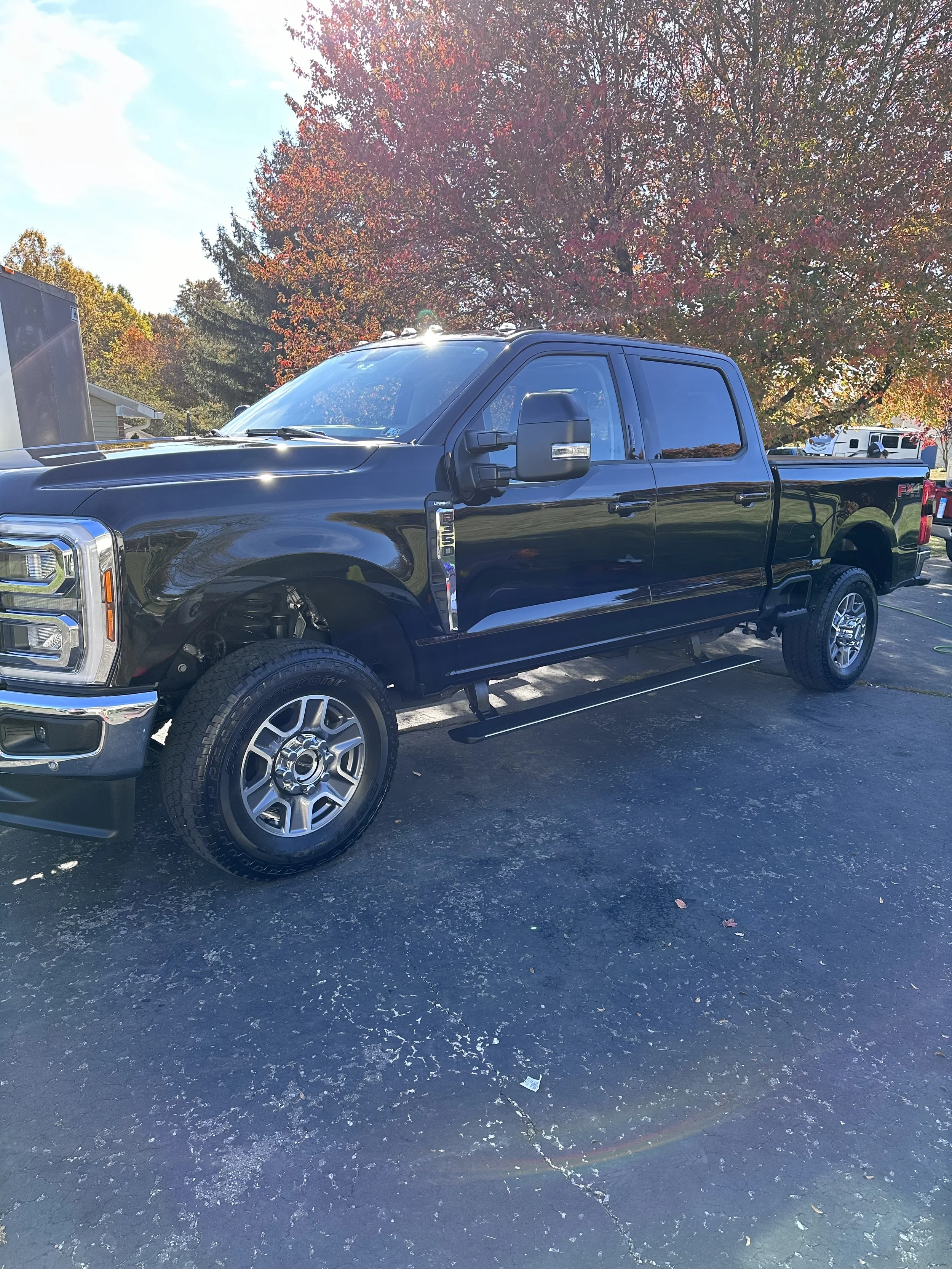 Black Ford F-350 pickup truck parked on a paved lot with autumn trees in the background.