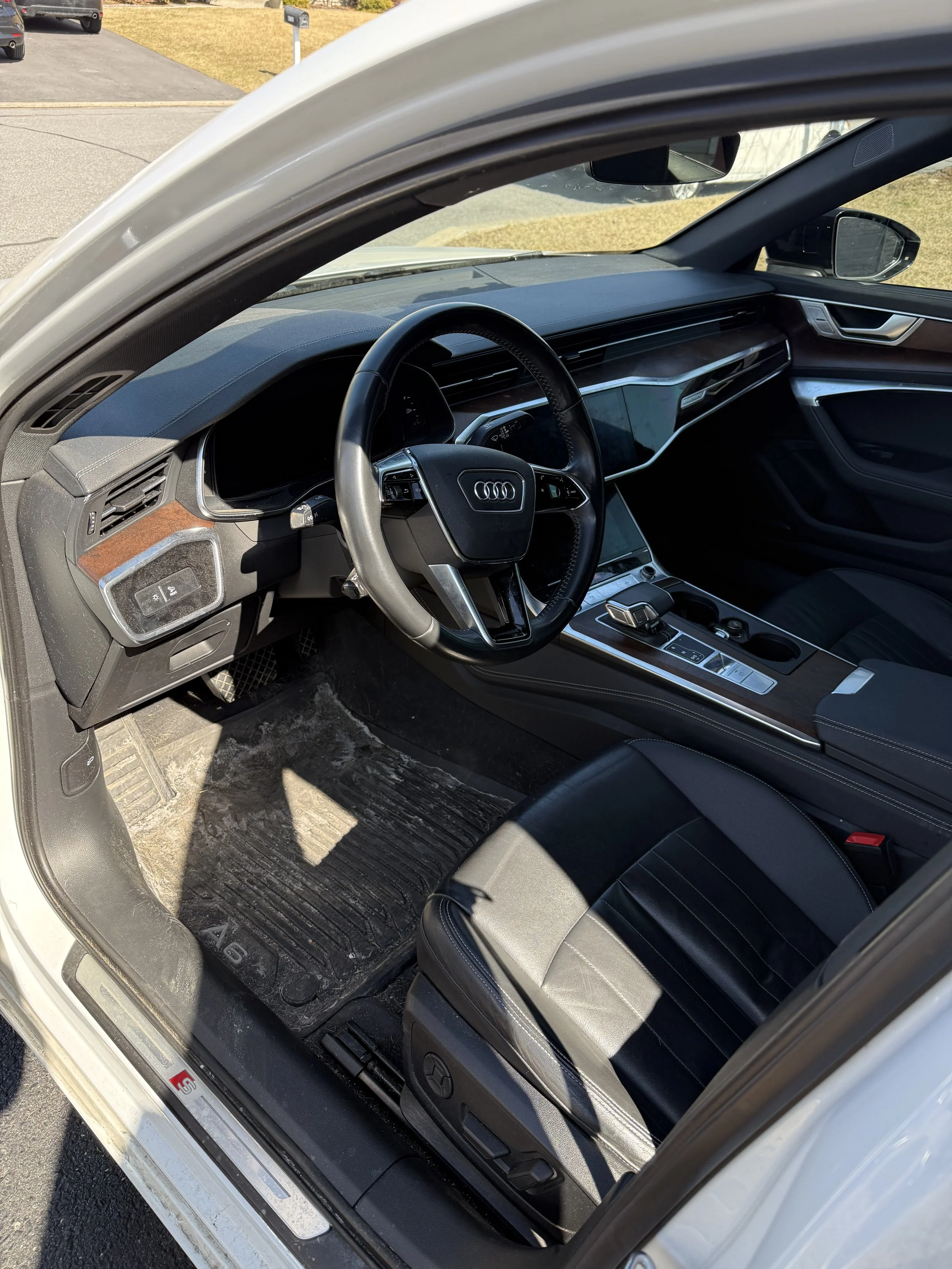 The interior of a white luxury car, showing the driver's side with a steering wheel, dashboard, center console, and black leather seat.