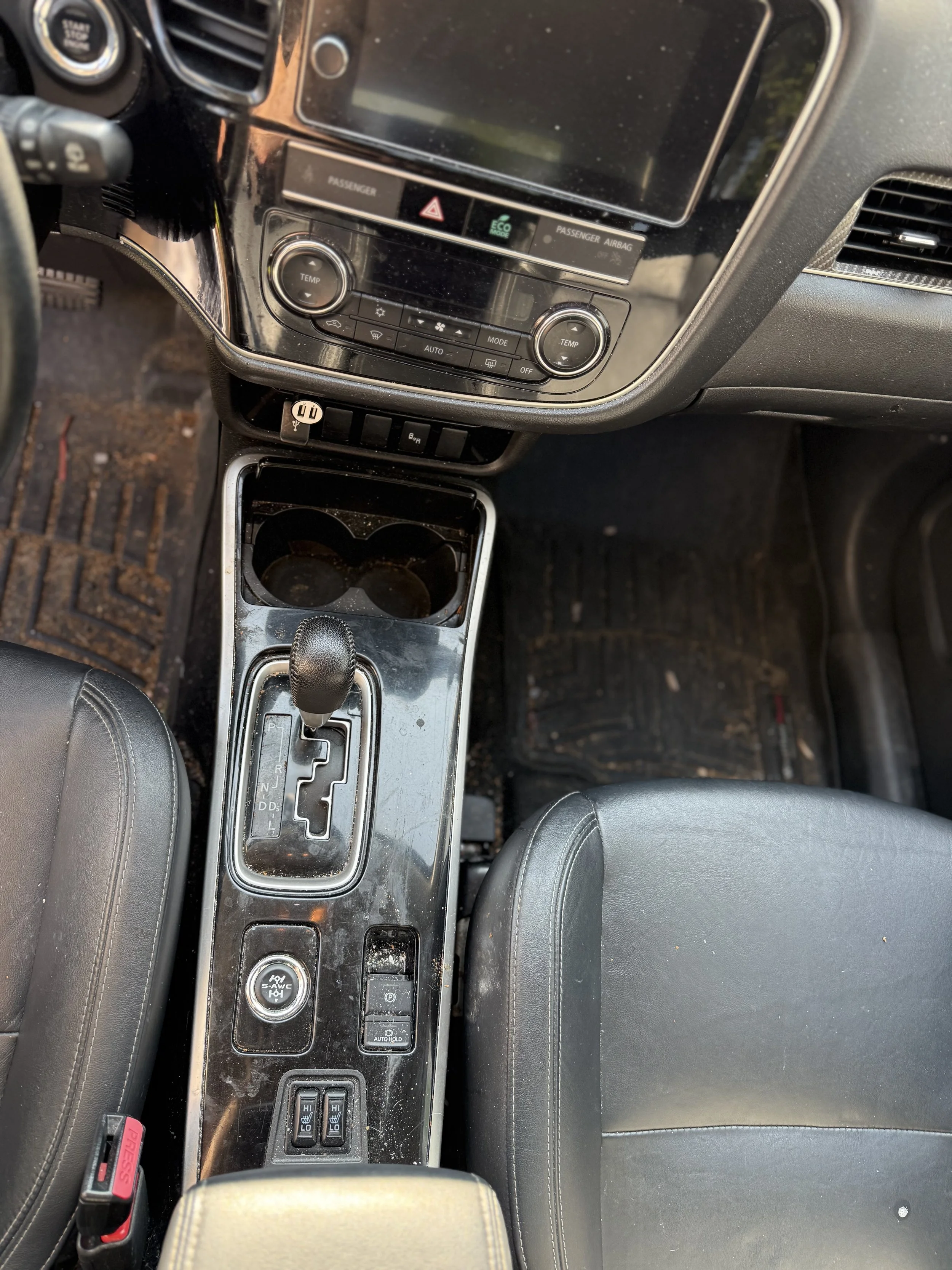 Inside view of a car's center console showing the gear shift, cup holders, and dashboard controls.