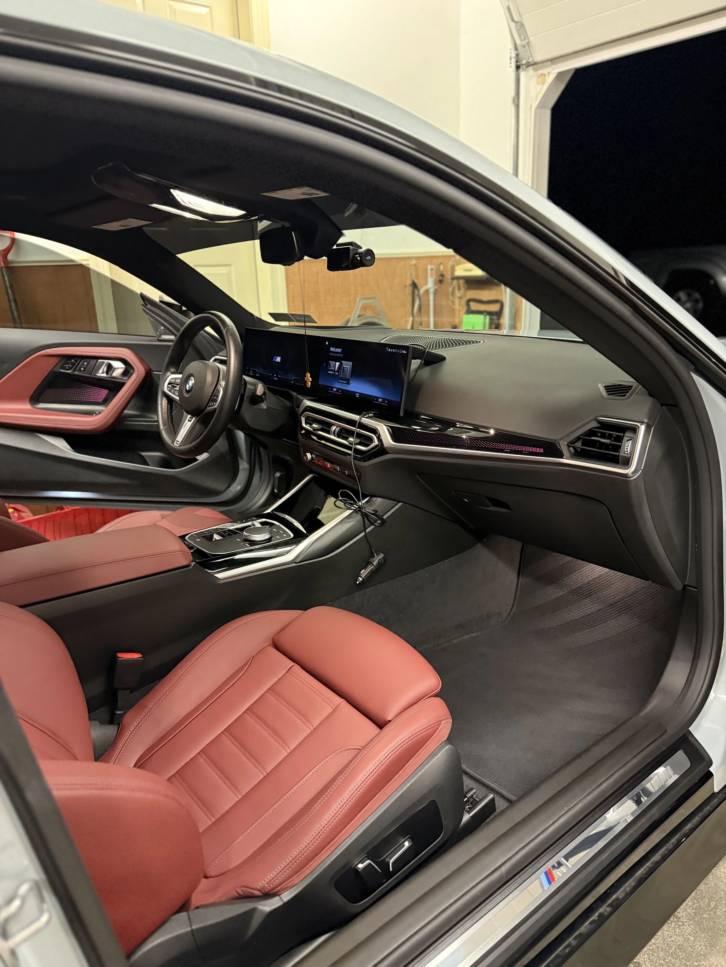 The interior of a BMW car with red seats, a digital dashboard display, steering wheel, gear shift, and a center console, inside a garage.