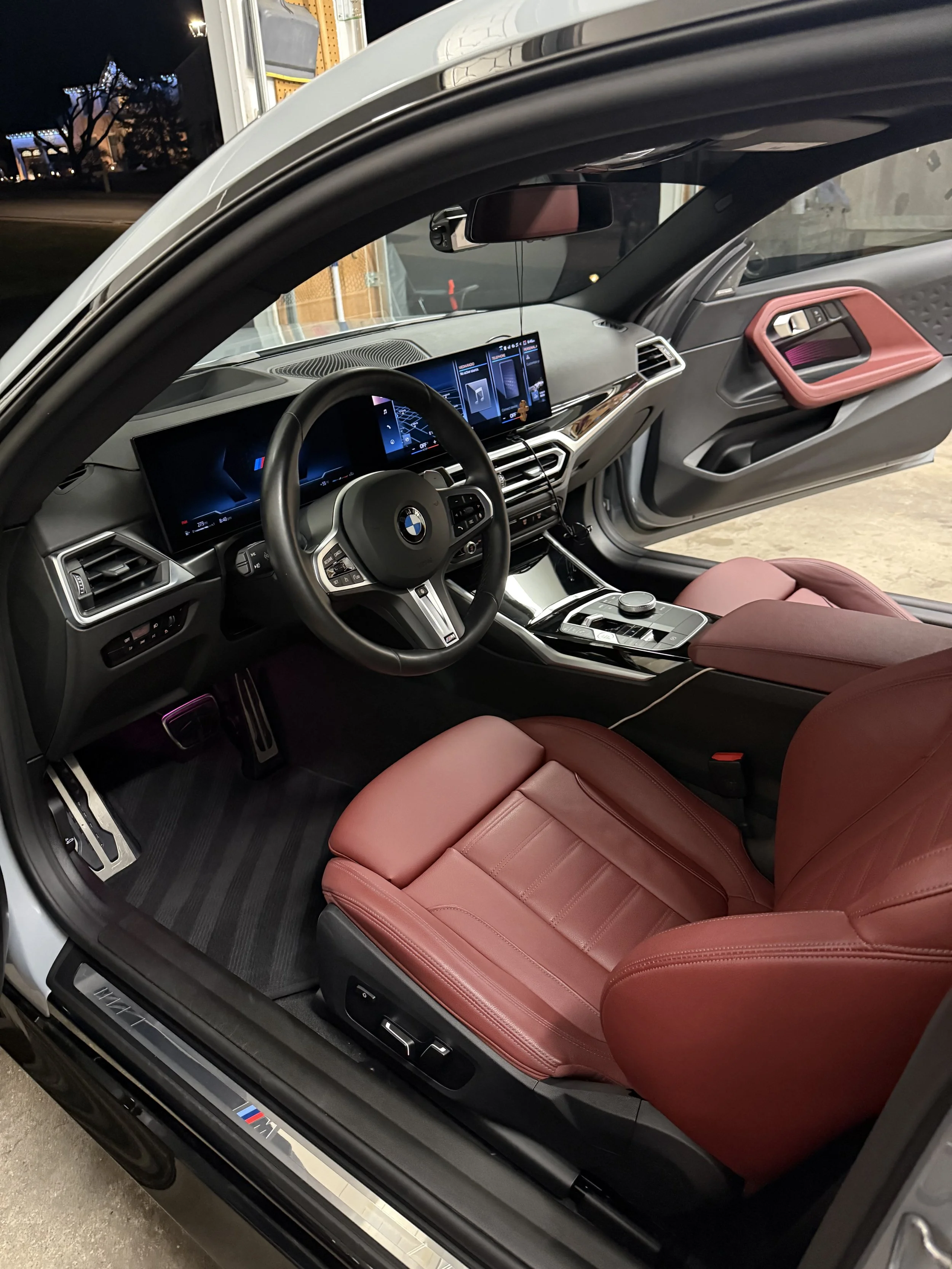 Interior of a BMW vehicle with red leather seats, digital dashboard, and a large infotainment screen, taken from the driver's side door open.
